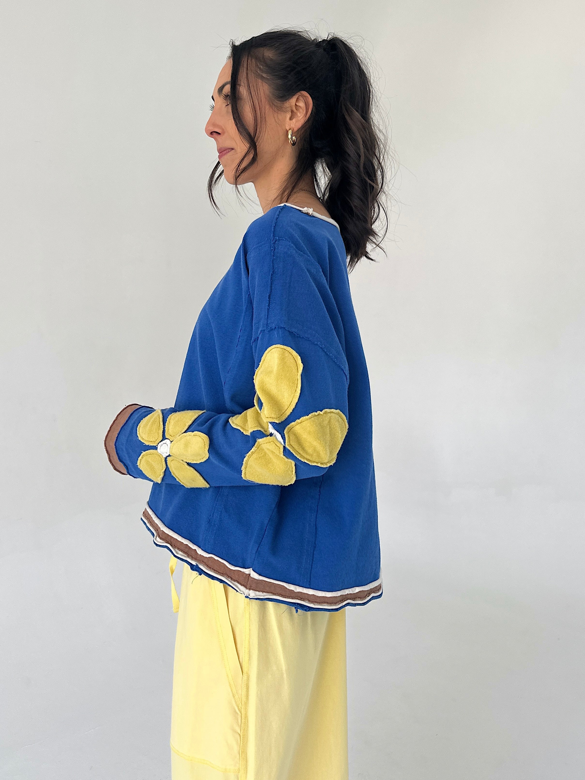 Person wearing a blue sweater with yellow floral patterns on a plain background