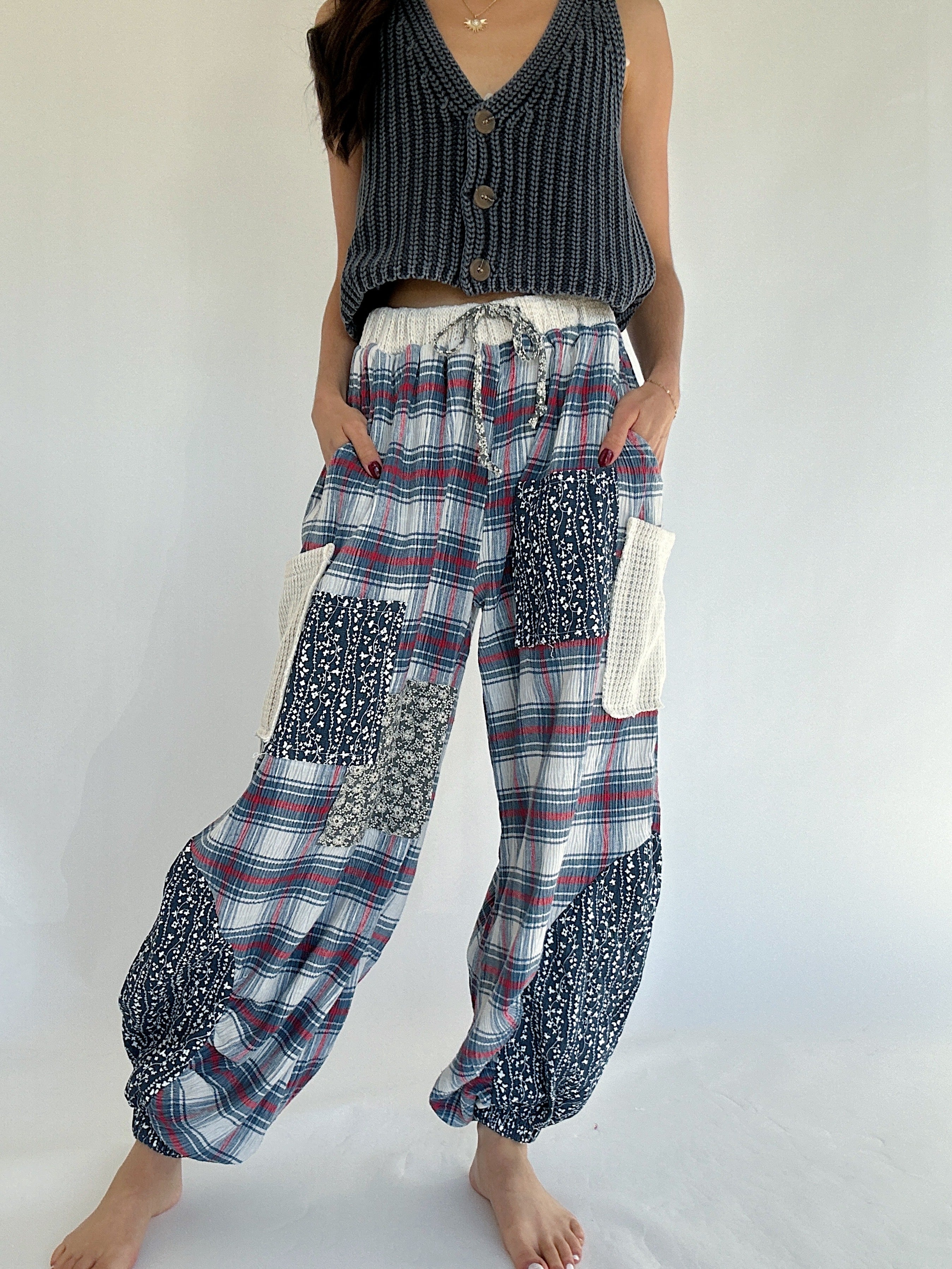 Person wearing a sleeveless top and plaid jogger style pants with a white background with no shoes on