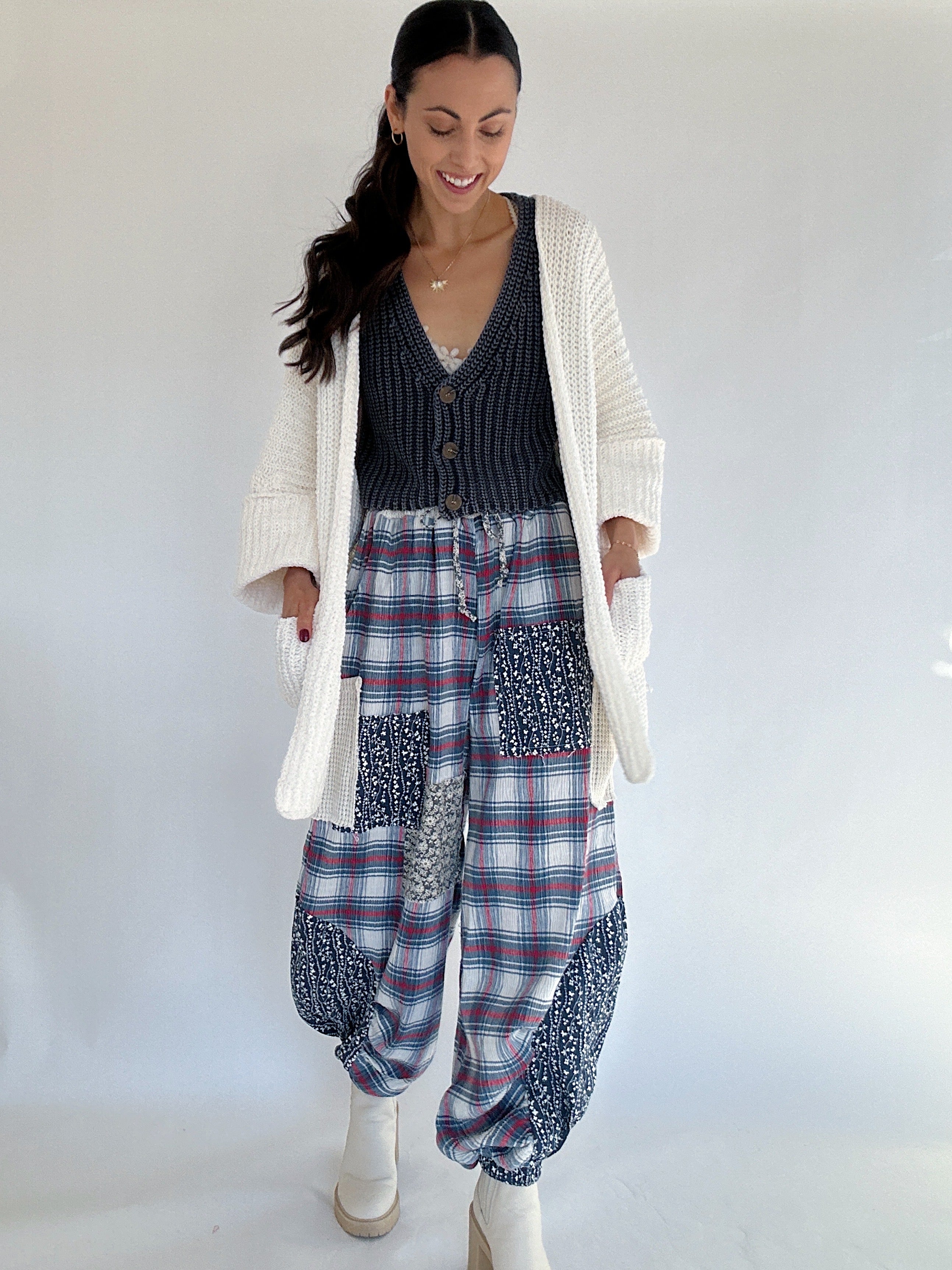 Woman wearing a plaid jogger pants with a white cardigan against a white background