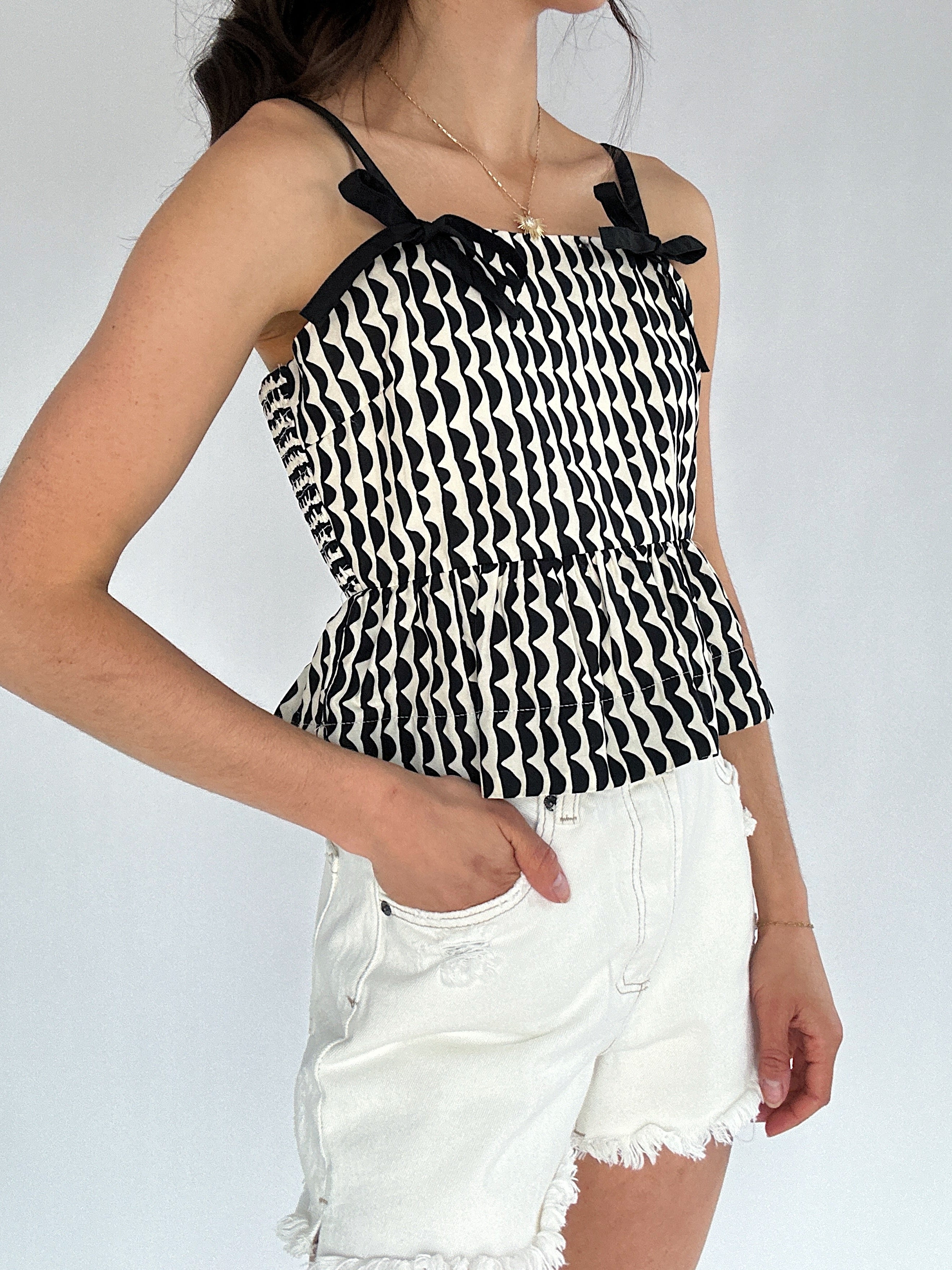 Person wearing a black and white patterned top with thin straps on a plain background
