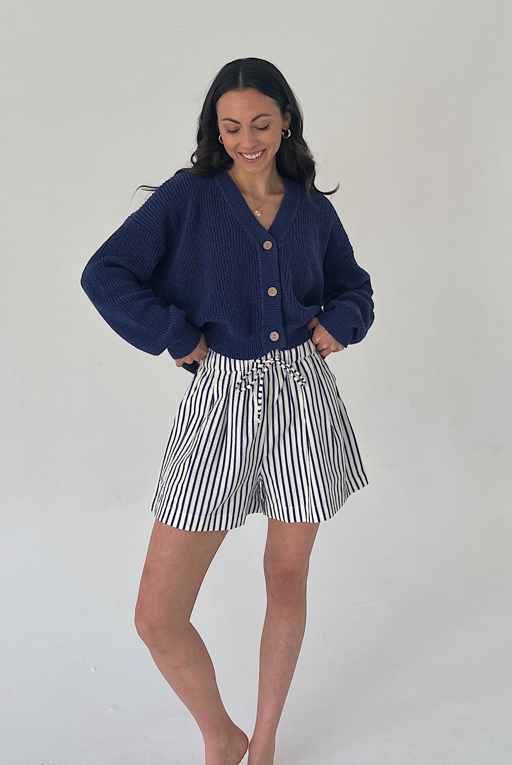 Woman wearing a navy cardigan and striped shorts on a plain background