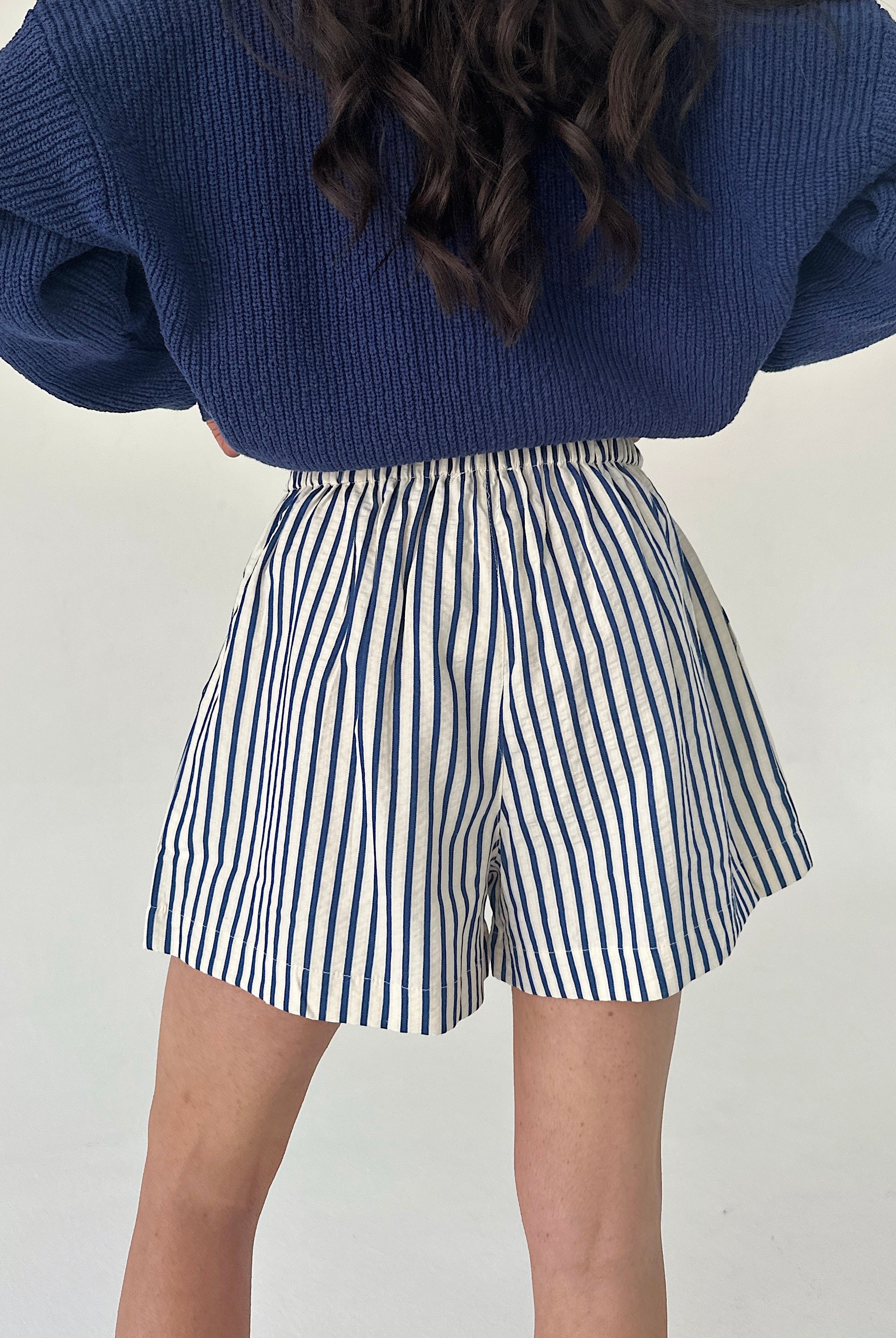 Person wearing blue sweater and striped shorts on a plain background from back