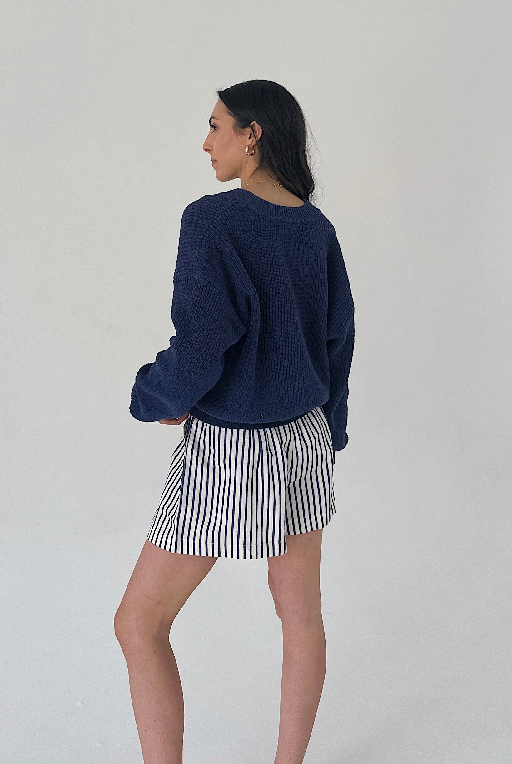 Woman wearing a navy sweater and striped skirt on a plain background