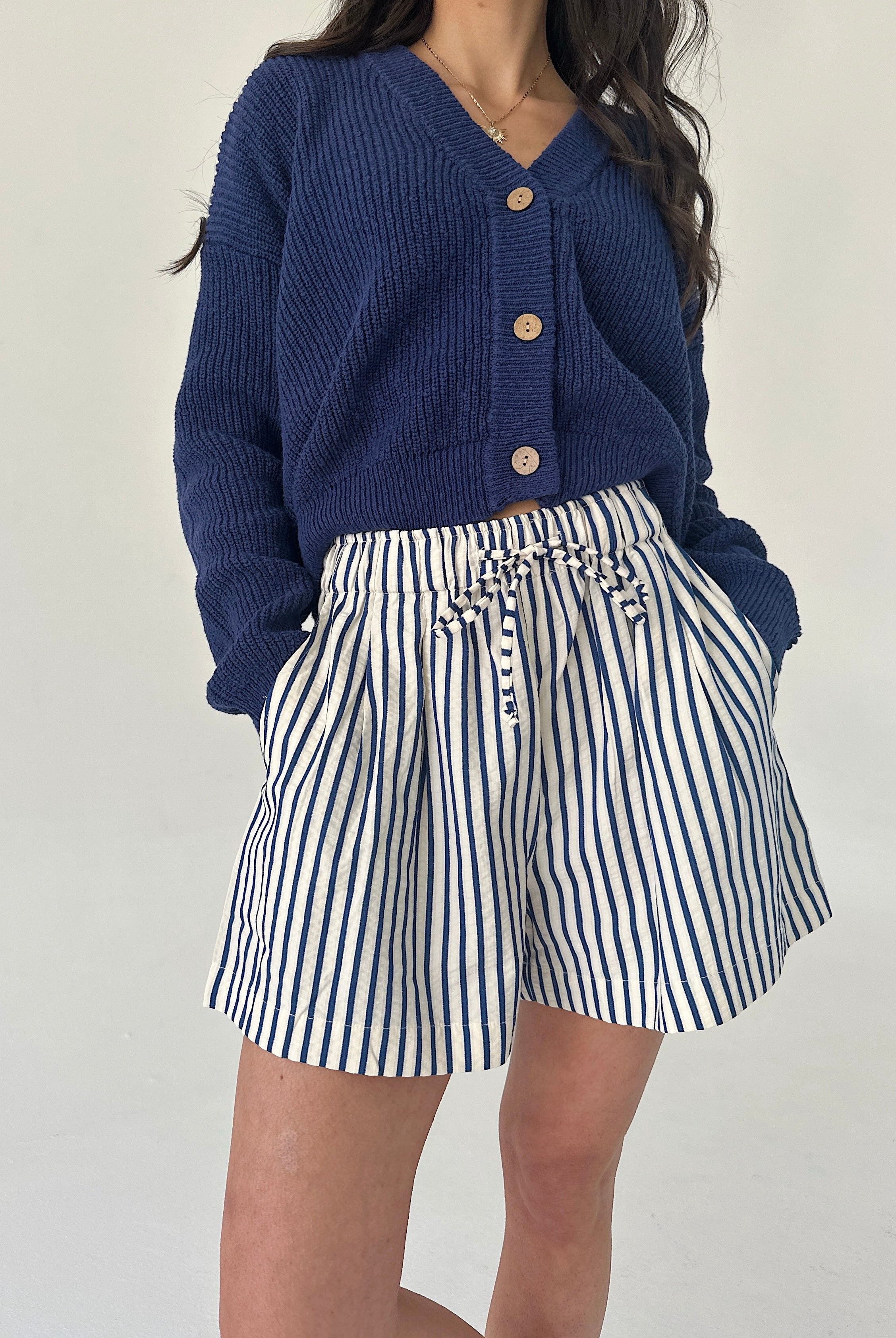 Person wearing a blue cardigan and striped shorts on a plain background