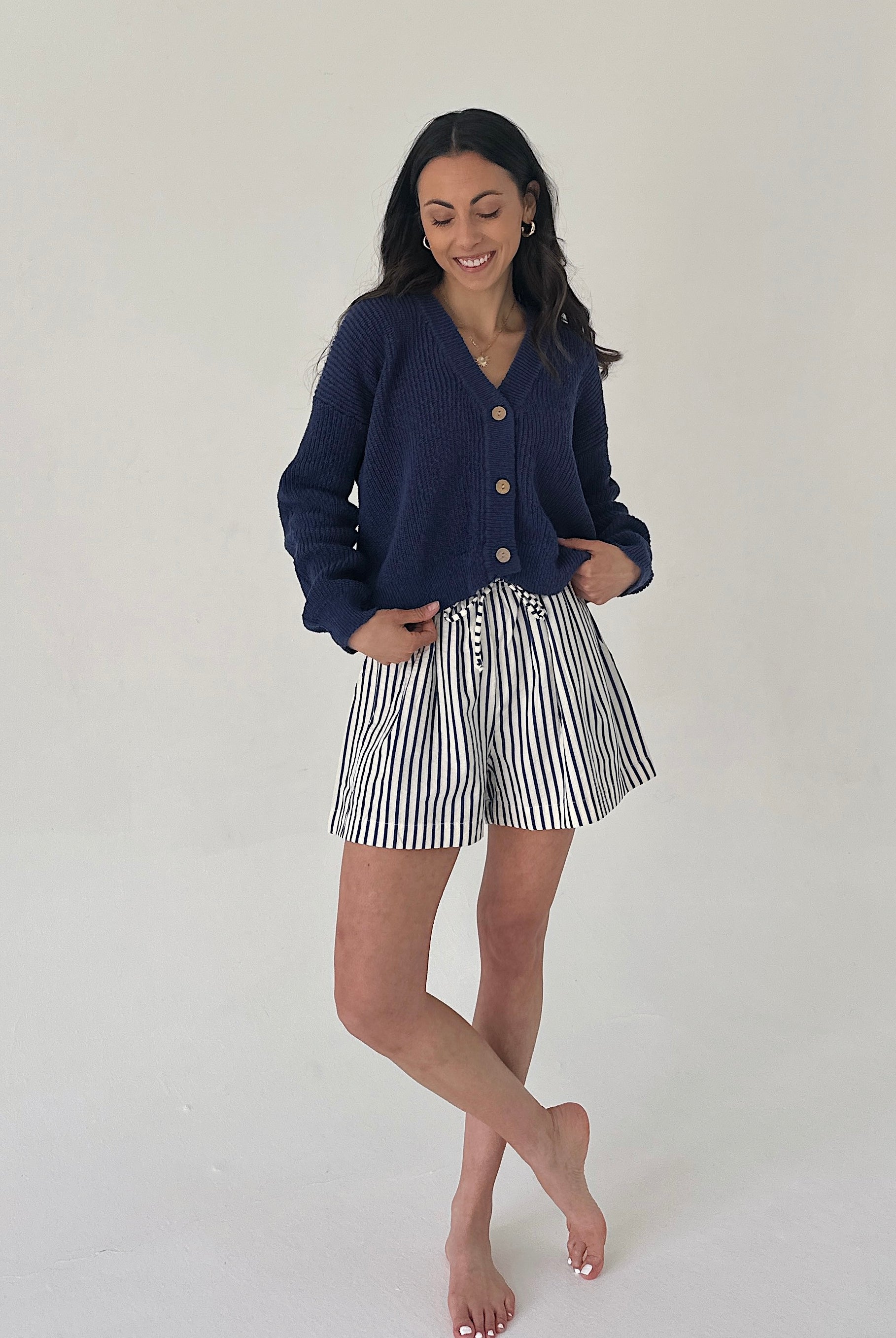 Woman wearing a navy cardigan and striped shorts on a plain background