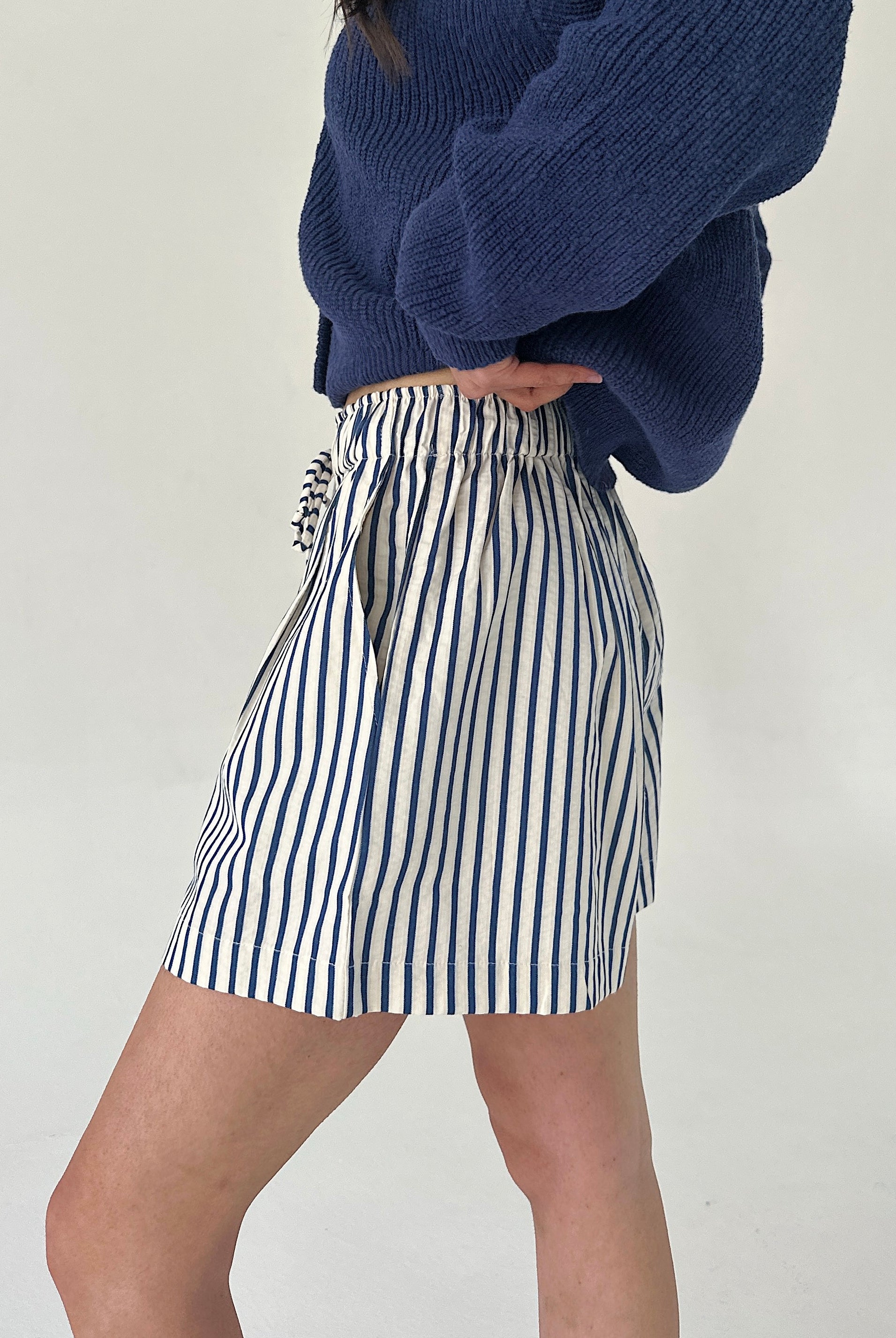 Person wearing a blue sweater and striped skirt on a plain background