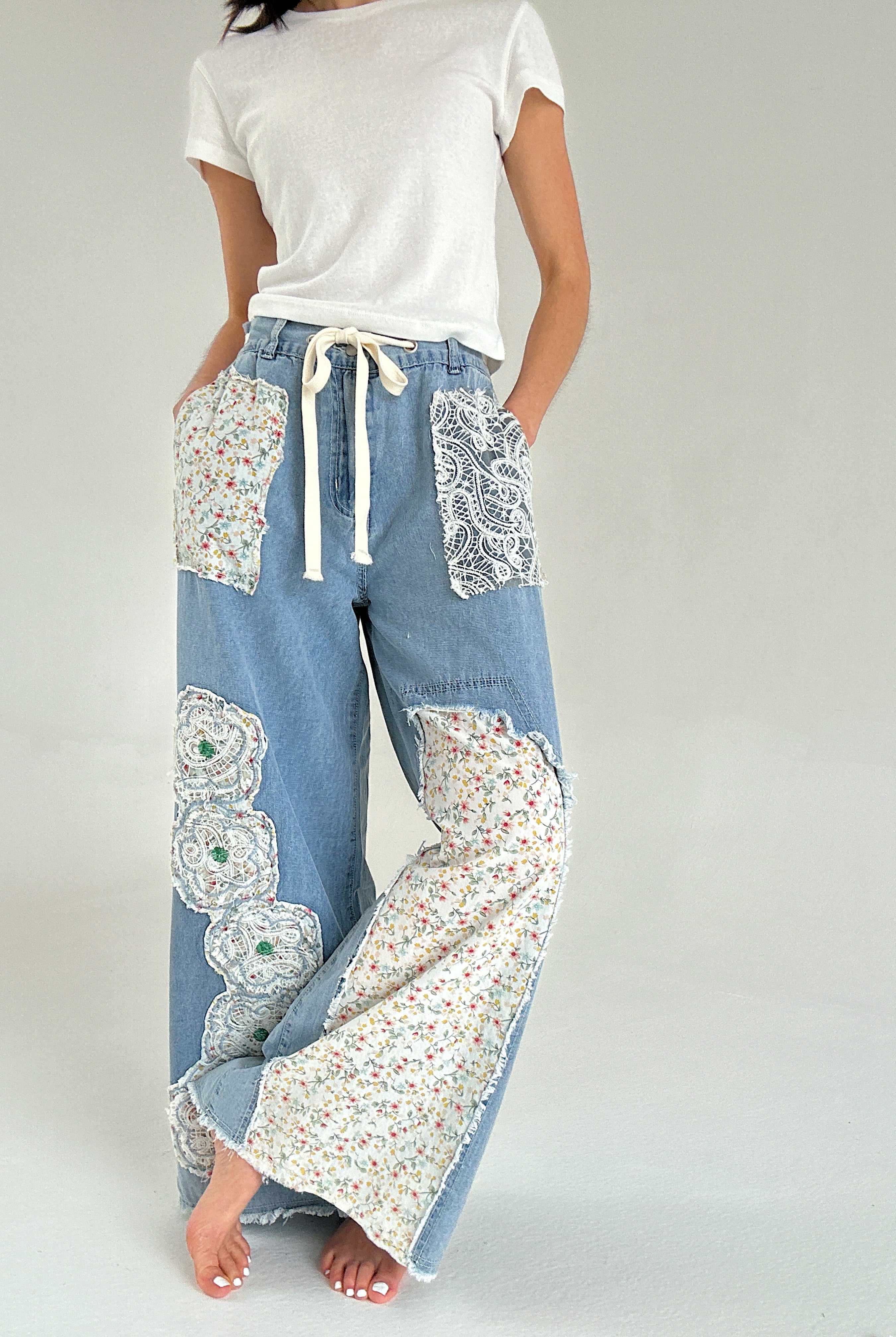 Person wearing light blue denim pants with floral patchwork on a plain background