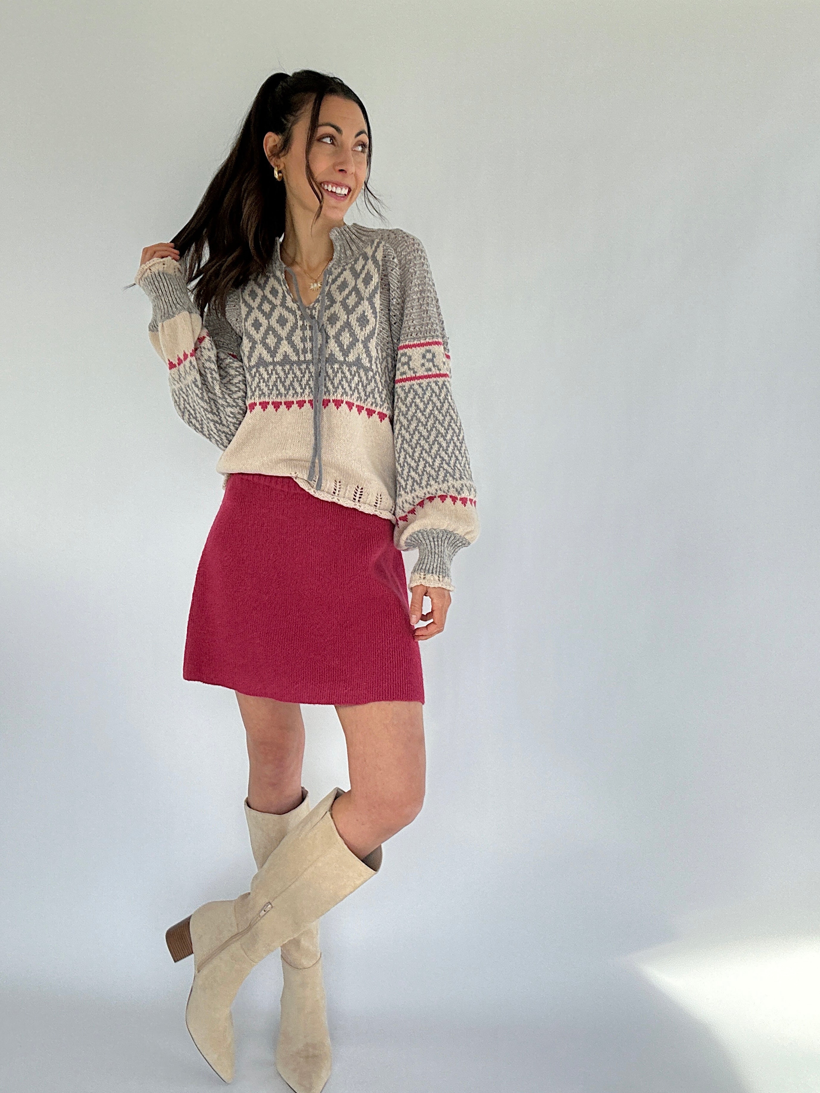 Woman wearing a patterned sweater, red skirt, and beige knee-high boots against a white background