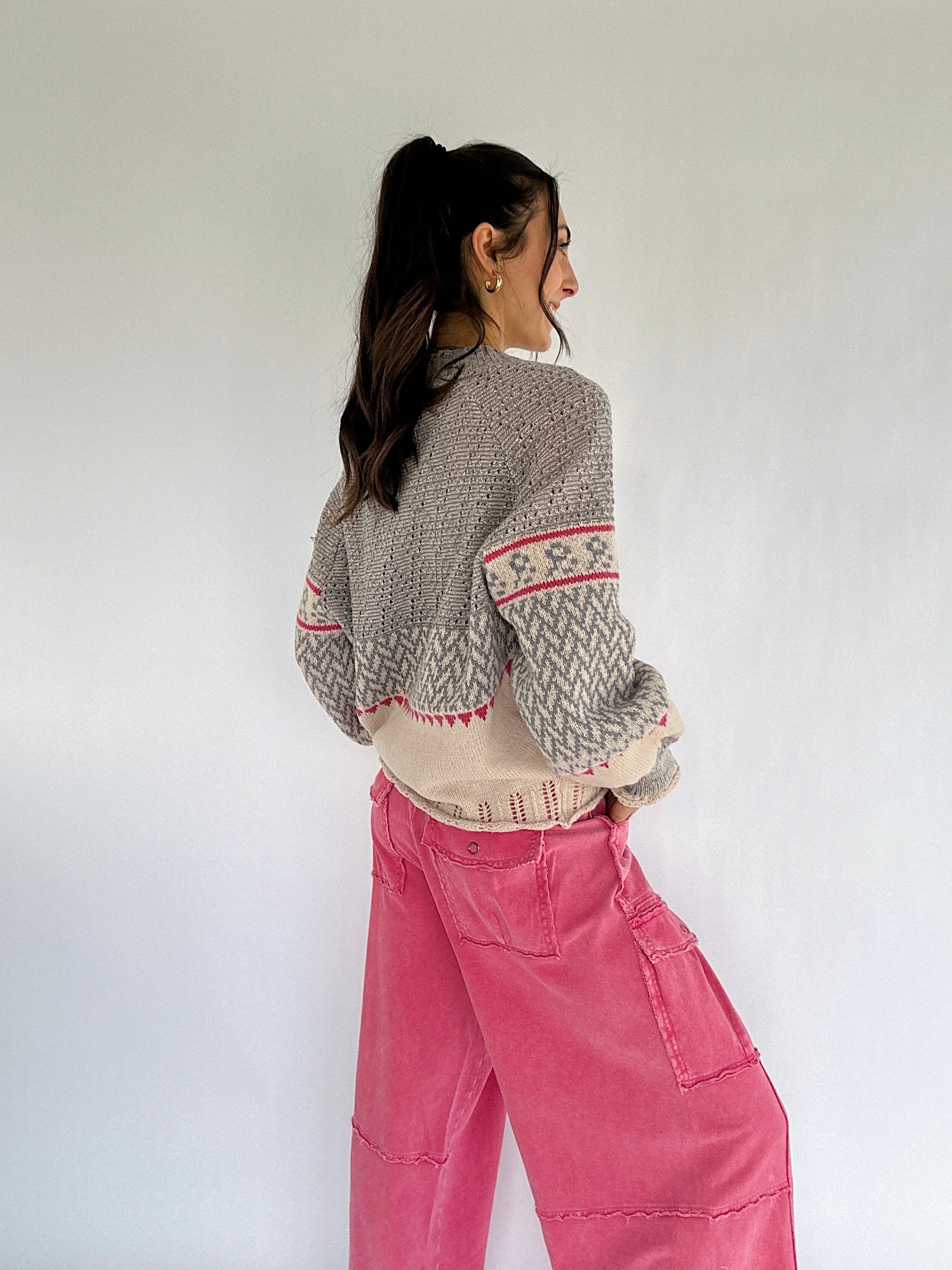 Person wearing a patterned sweater and pink pants against a white background