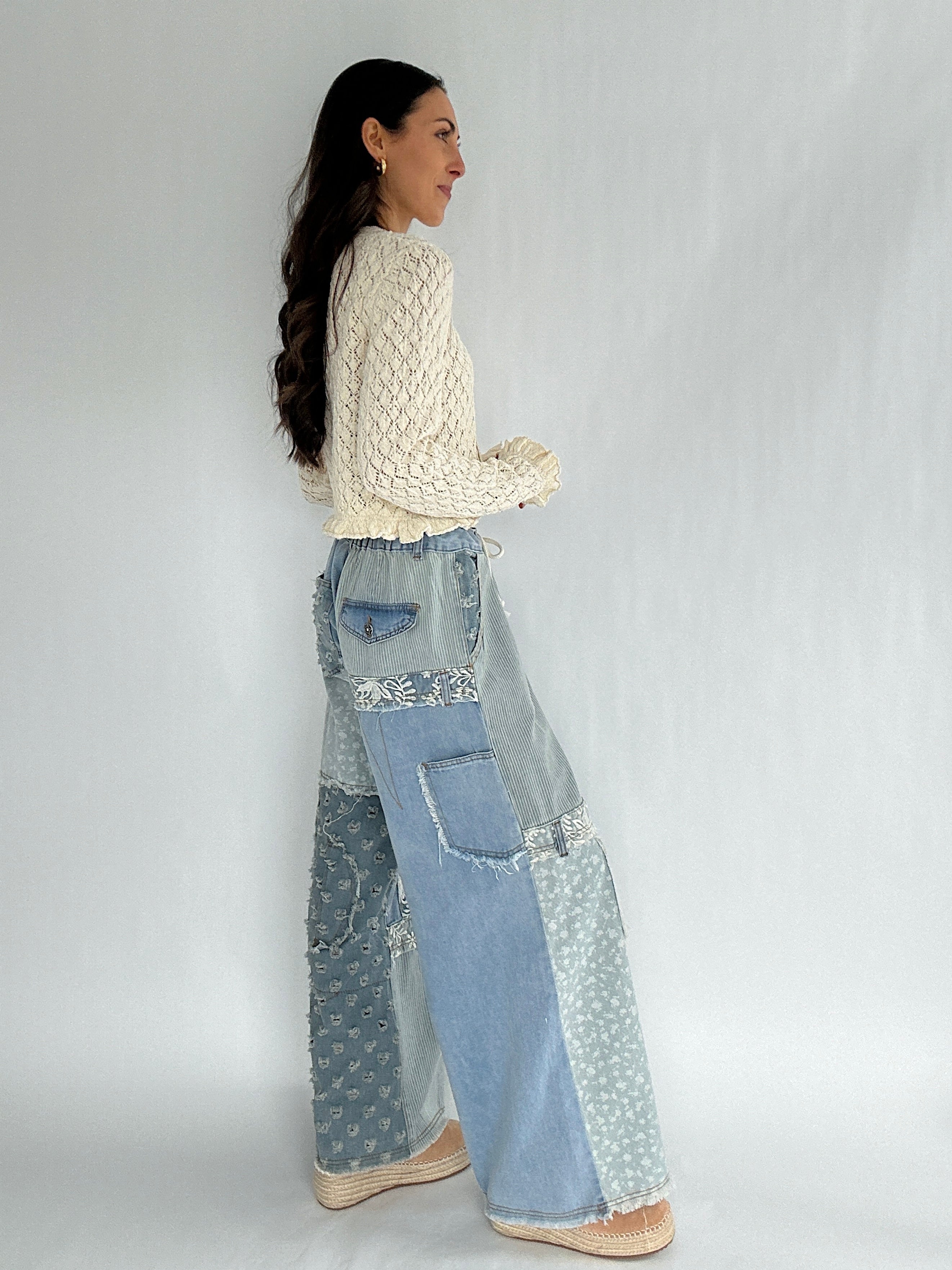 Woman wearing a cream sweater and patchwork jeans on a white background