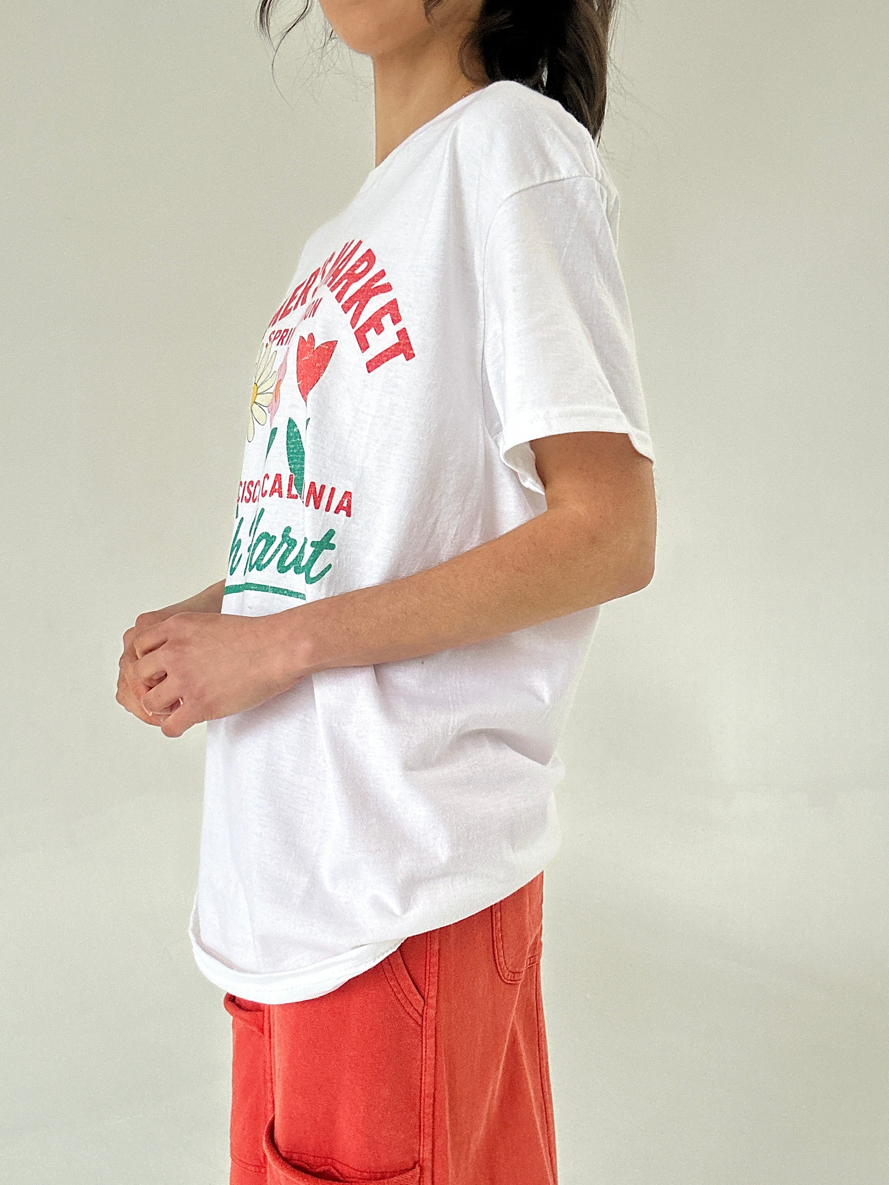 Person wearing a white t-shirt with colorful graphics and text on a plain background