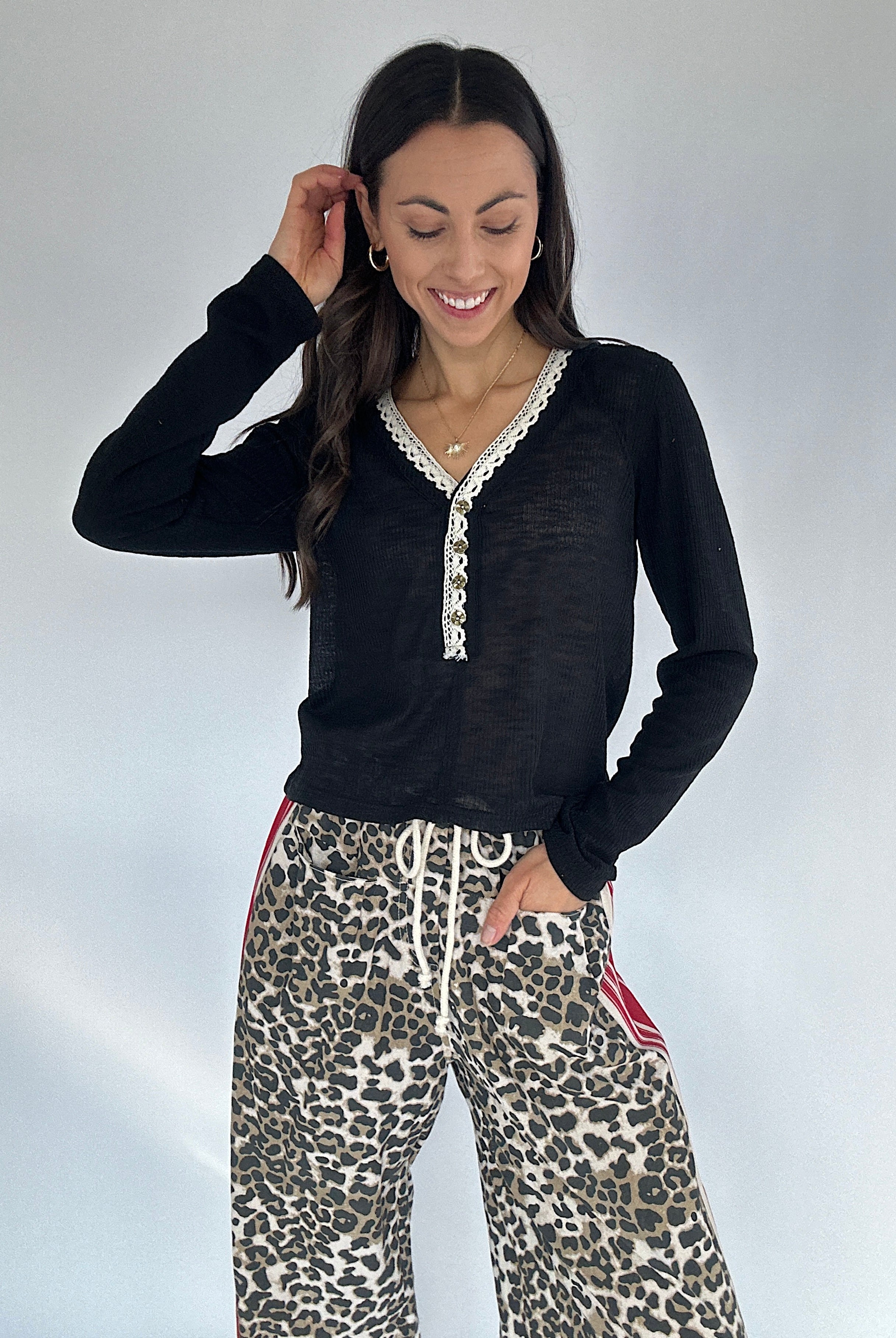 Woman wearing a black long-sleeve top with lace trim and leopard print pants against a white background