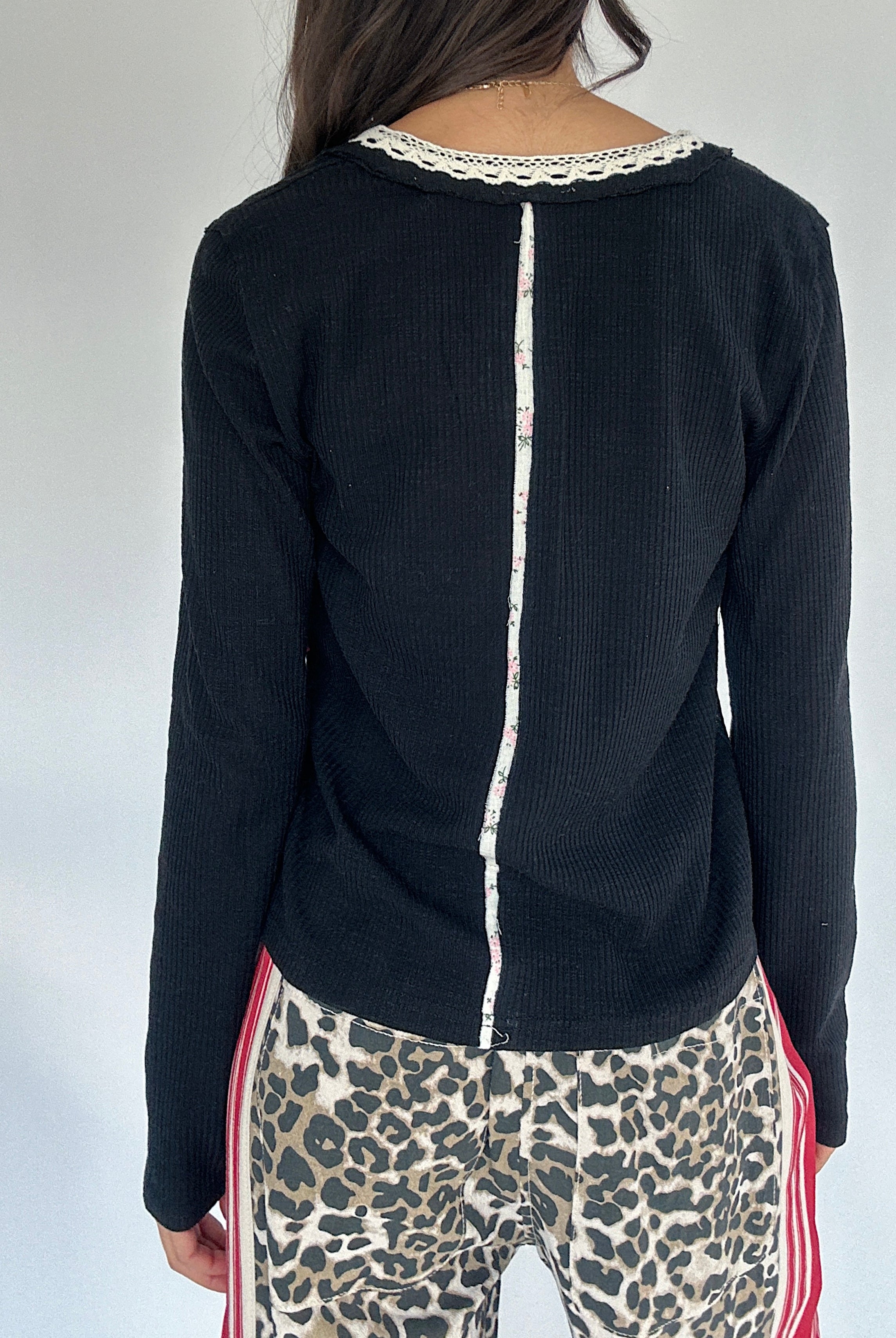 Person wearing a black long-sleeve top with white trim down the back and leopard print pants on a plain background