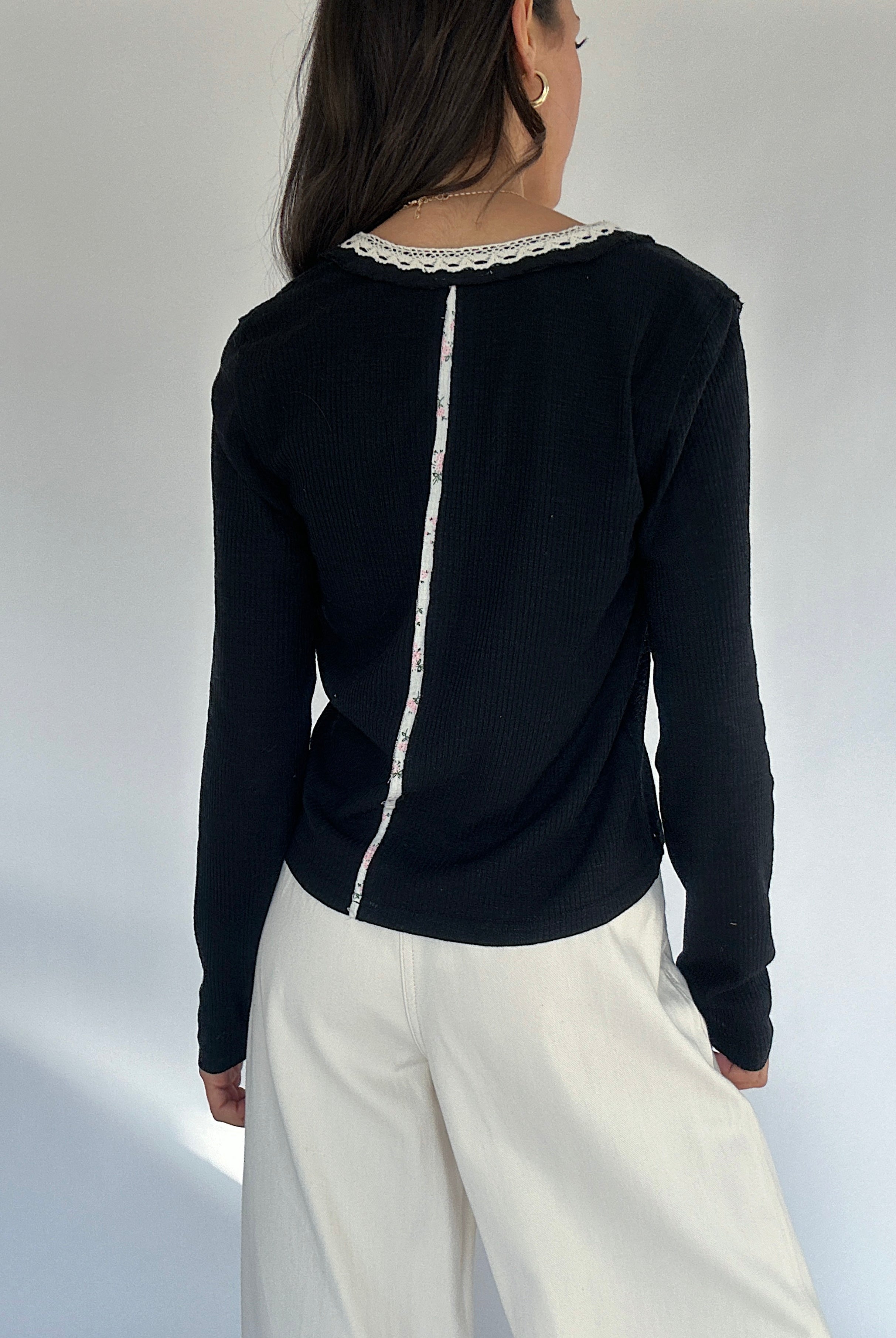Person wearing a black long-sleeve top with white lace trim on a plain background