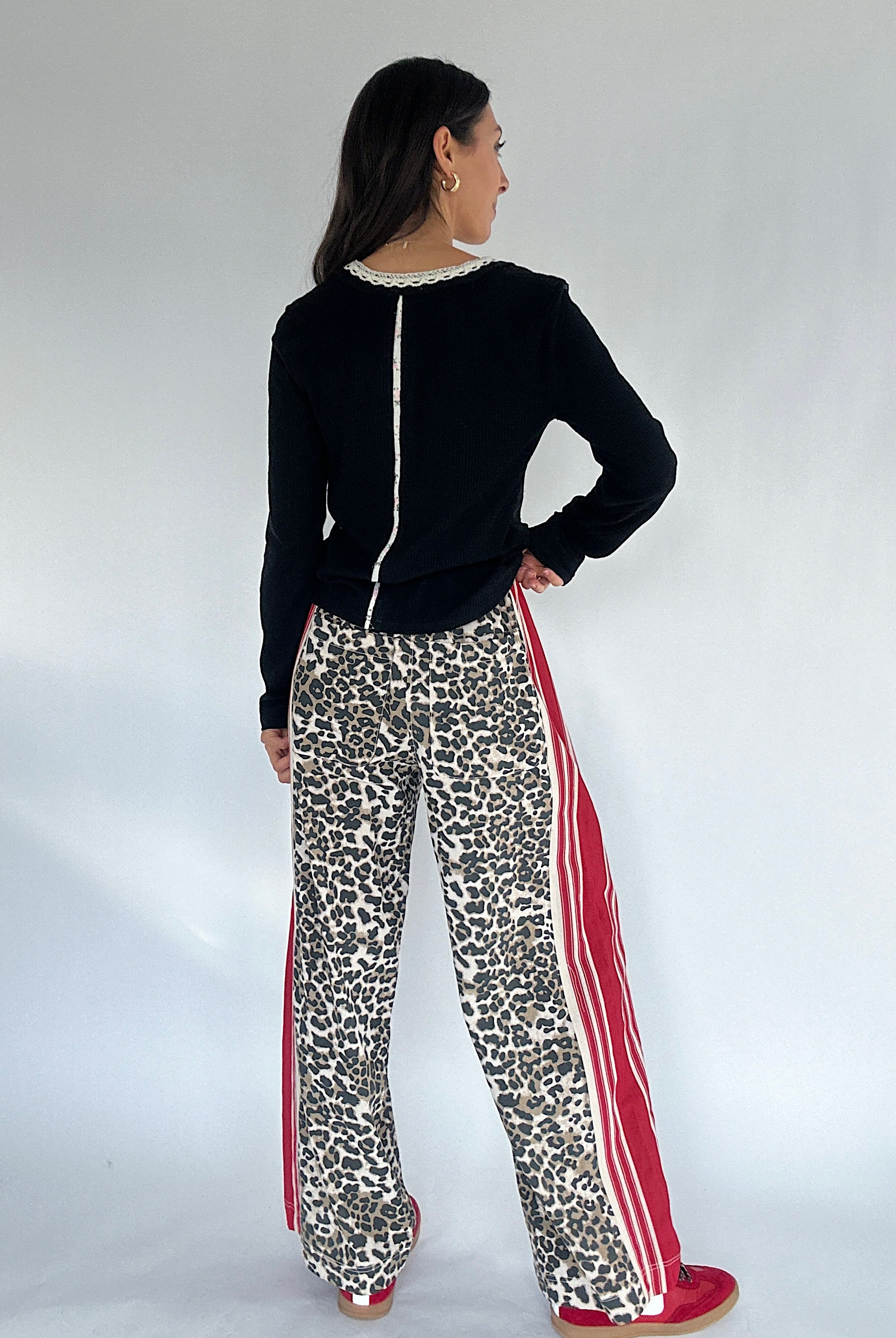 Woman wearing a black top and leopard print pants with red stripes on a white background