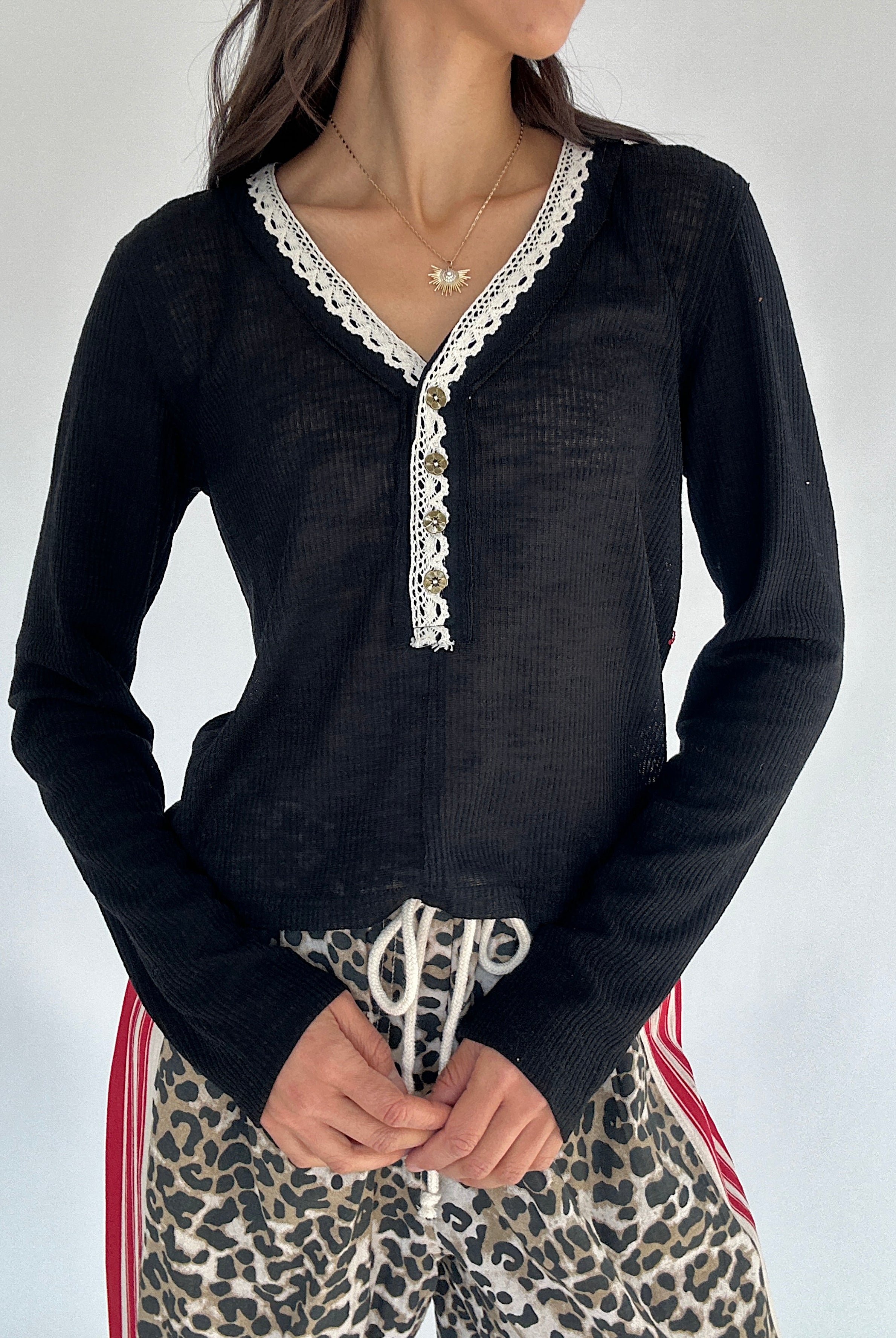 Person wearing a black long-sleeve top with lace trim and leopard print pants against a white background