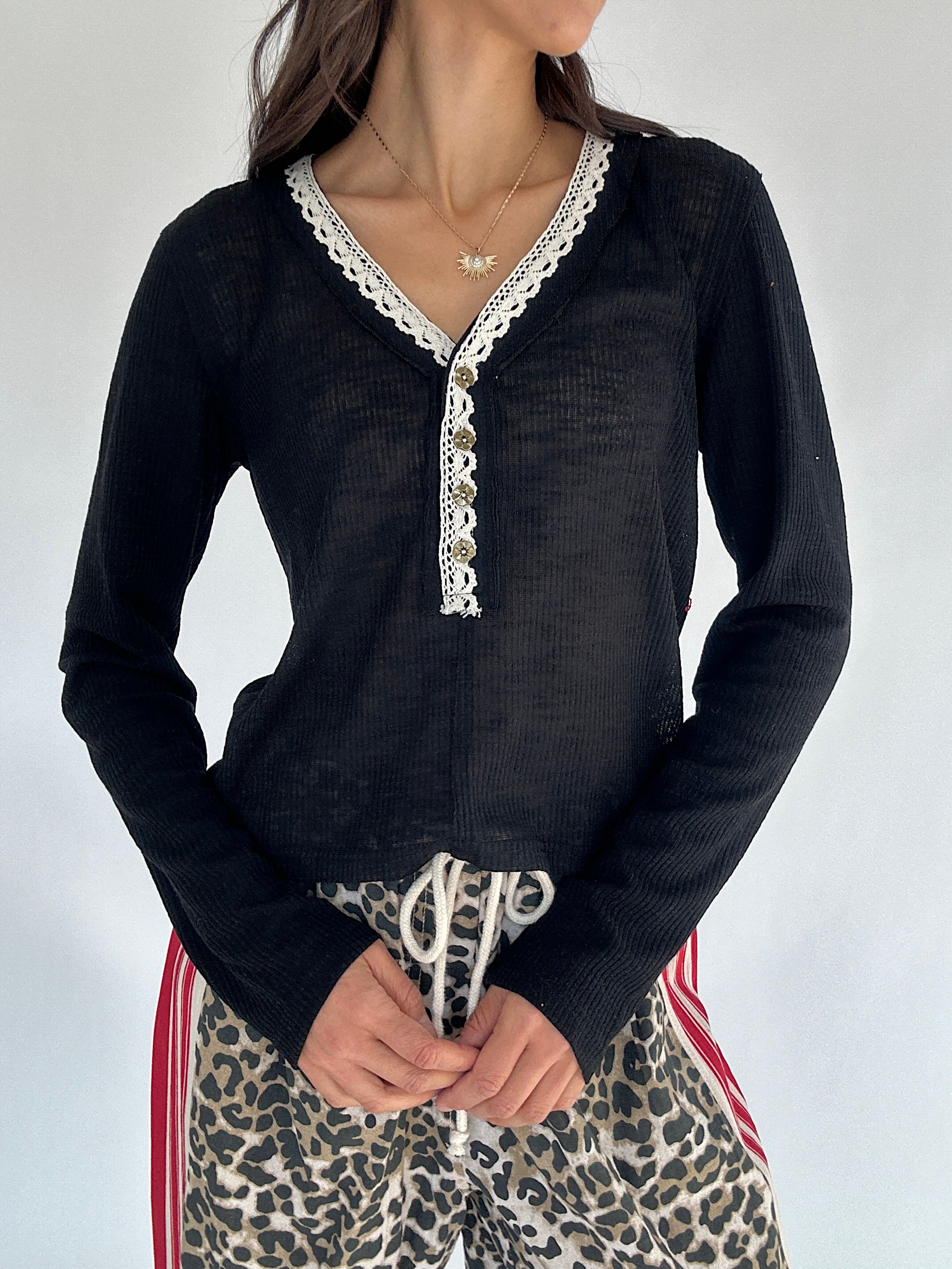 Person wearing a black long-sleeve top with lace trim and leopard print pants against a white background