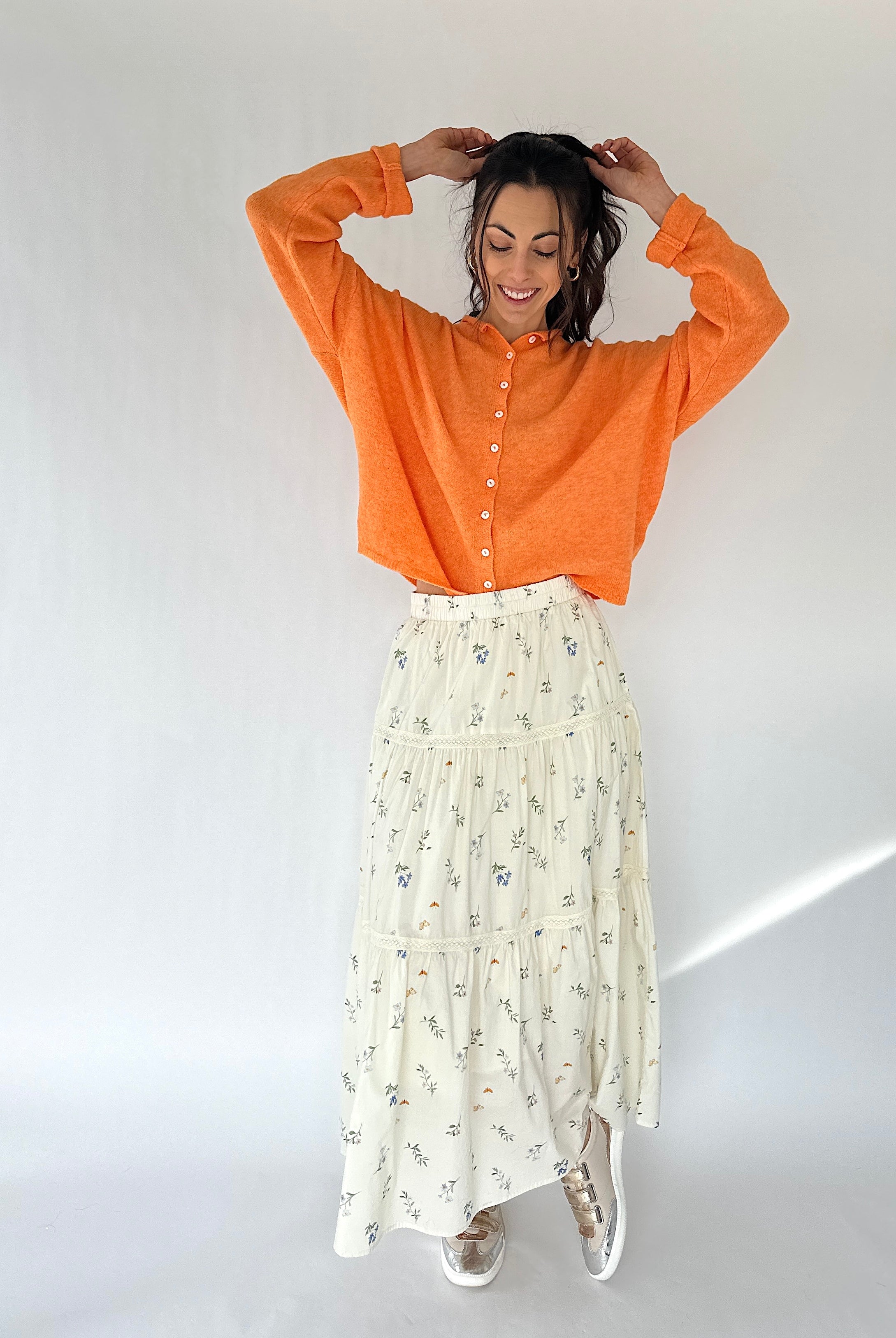 Woman wearing an orange shirt and white floral skirt against a white background