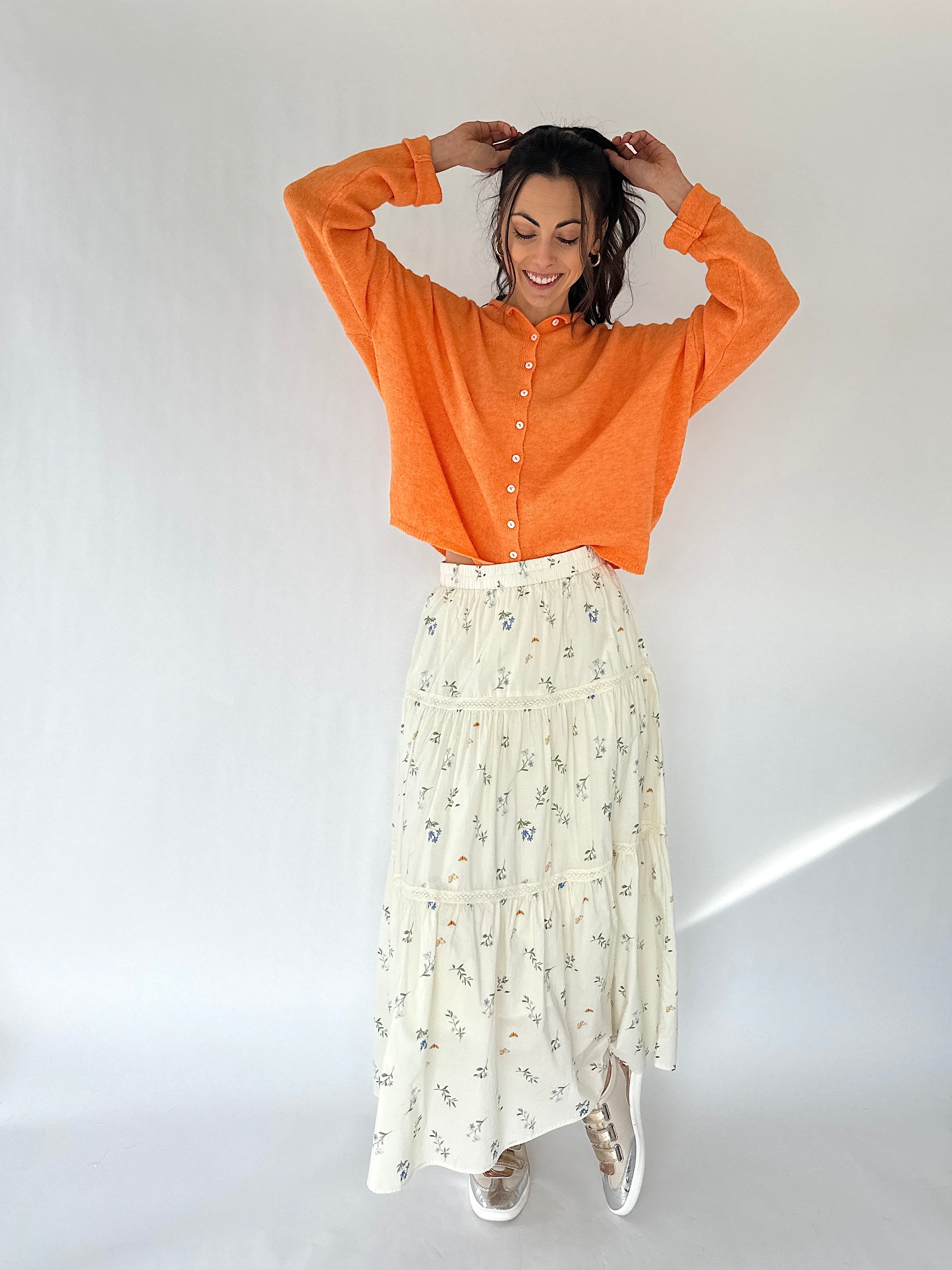 Woman wearing an orange shirt and white floral skirt against a white background