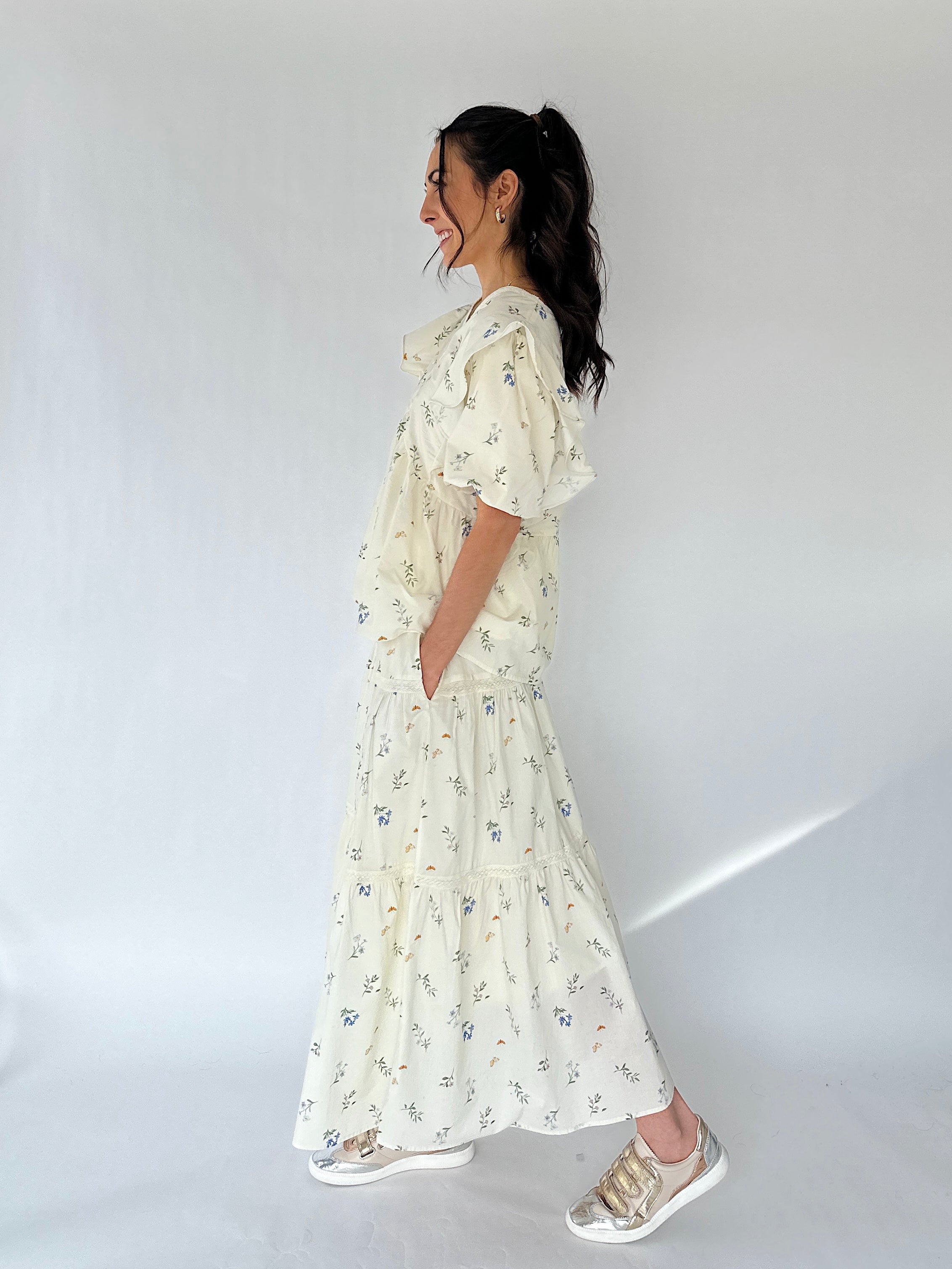 Woman wearing a white floral maxi skirt and matching top from side against a plain background