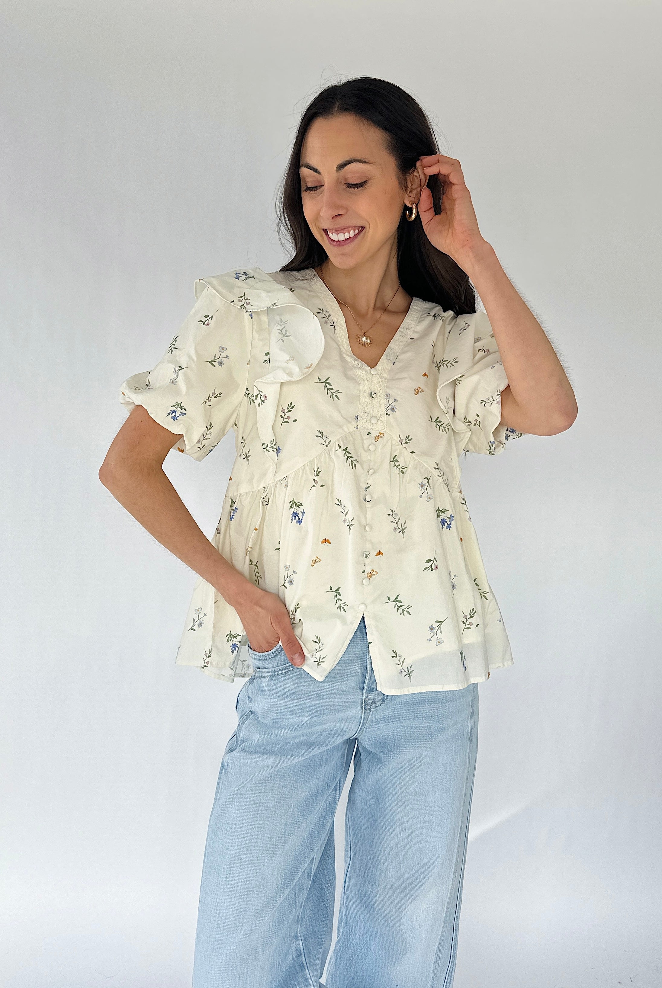 Woman wearing a floral blouse and light blue jeans against a white background