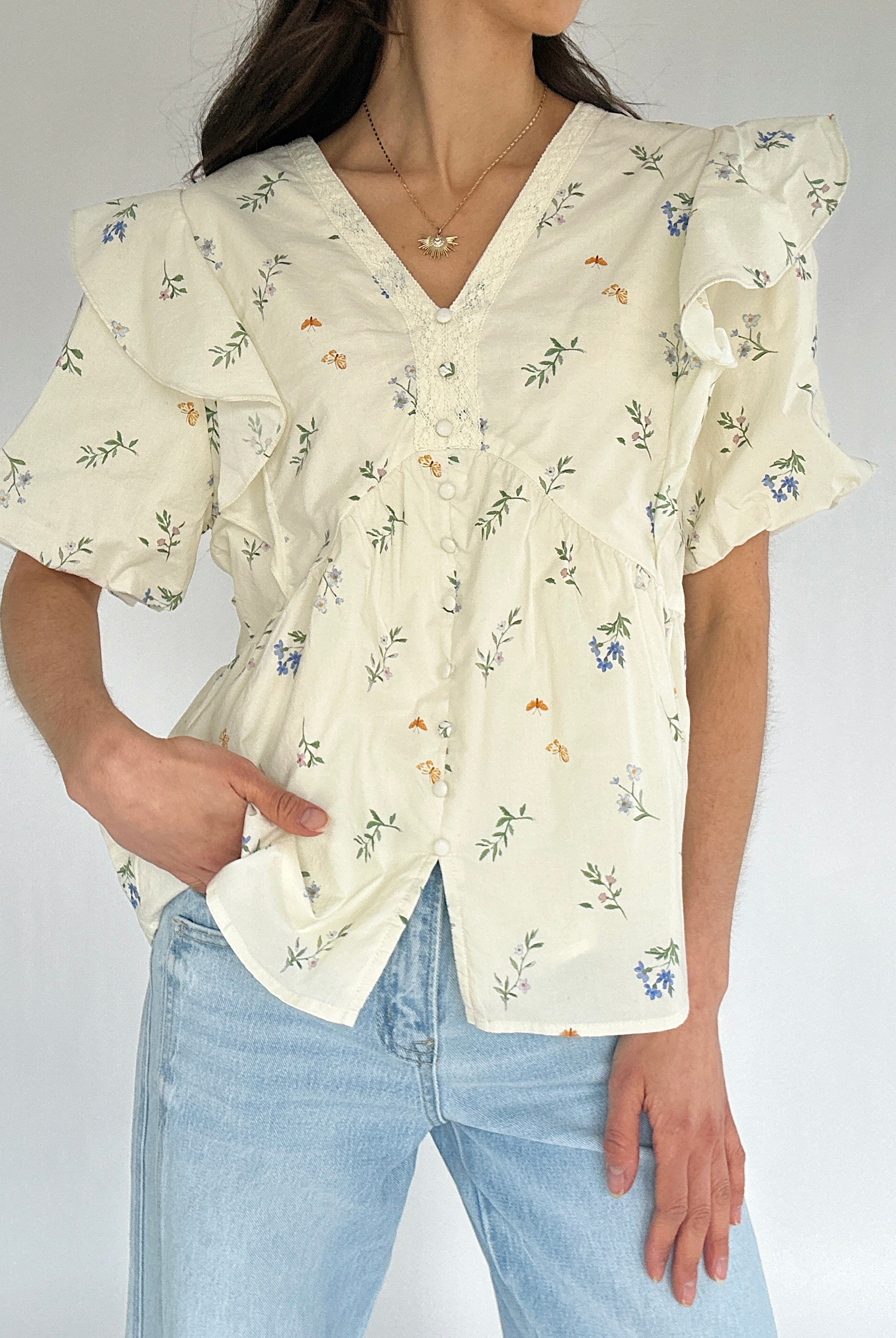 Woman wearing a floral blouse and light blue jeans against a plain background