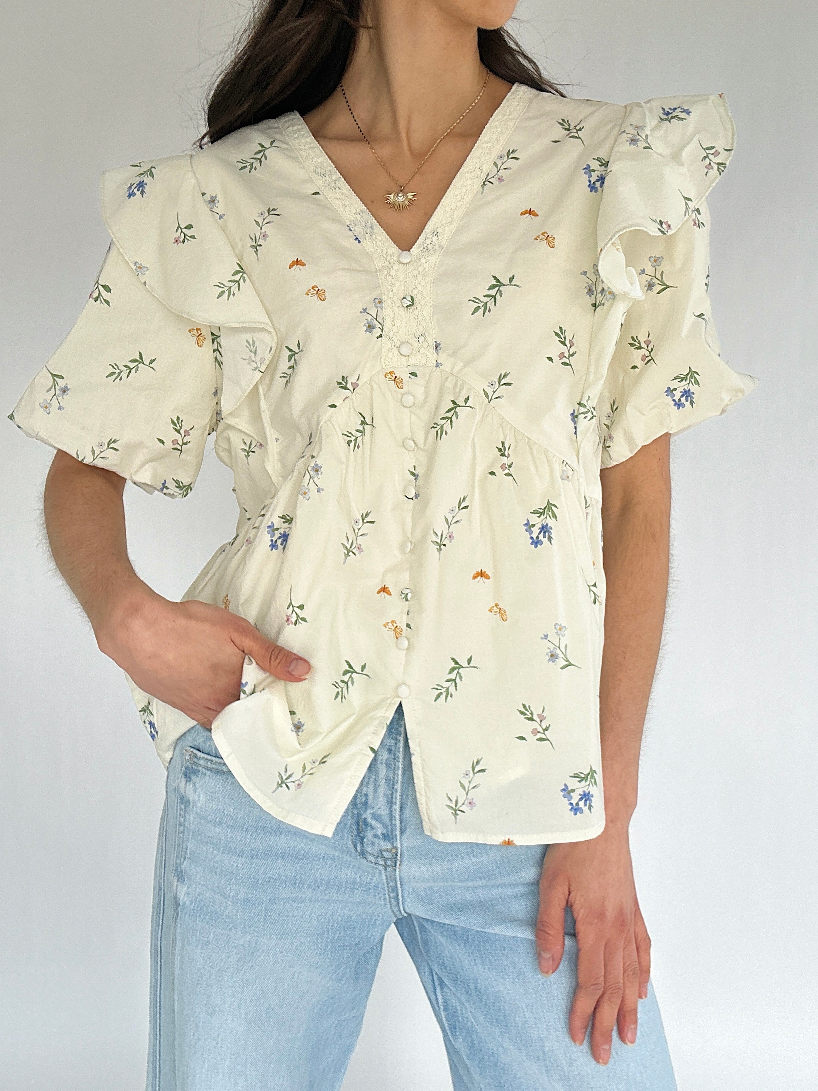 Woman wearing a floral blouse and light blue jeans against a plain background