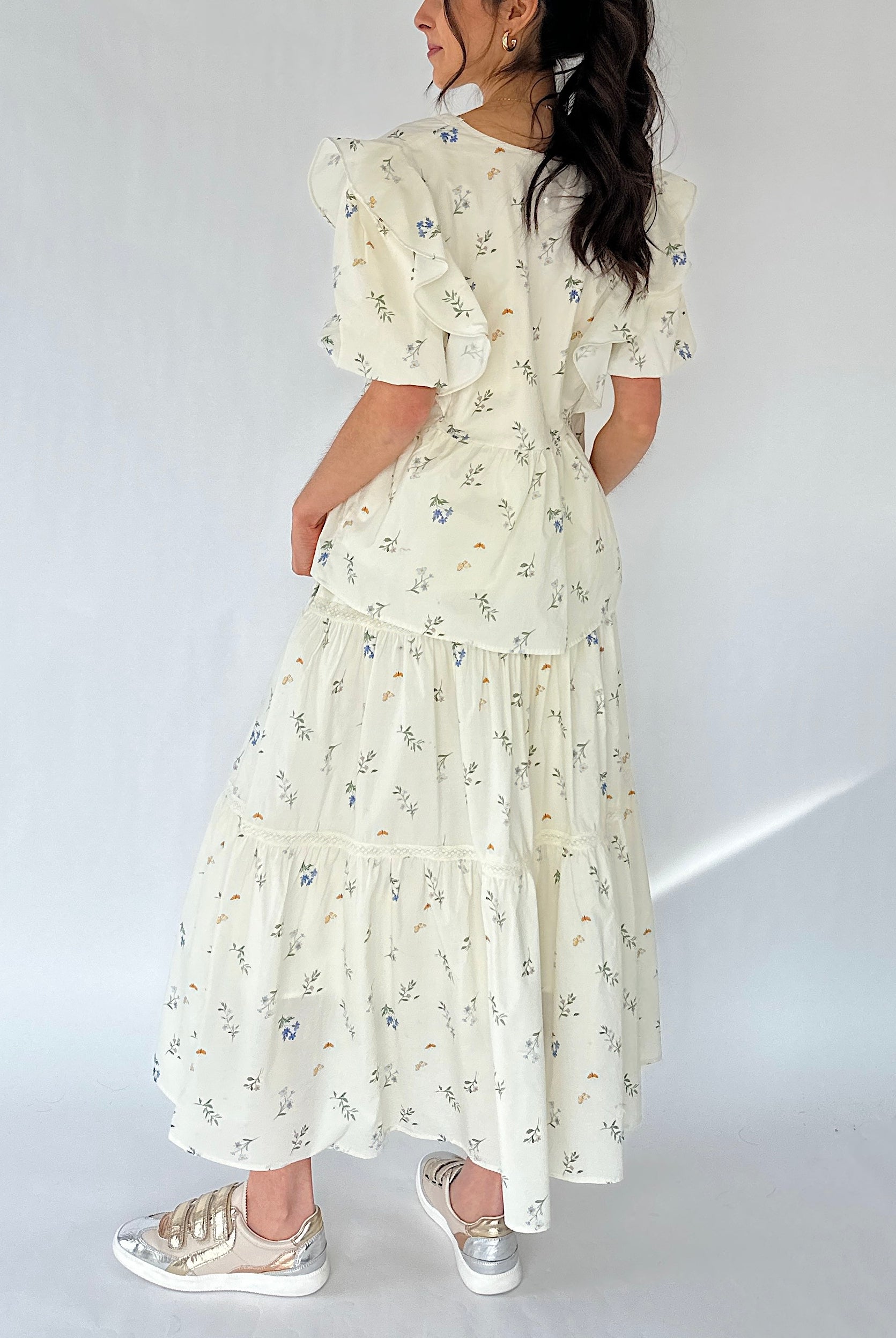 Woman wearing a floral maxi skirt and matching top from back on a white background