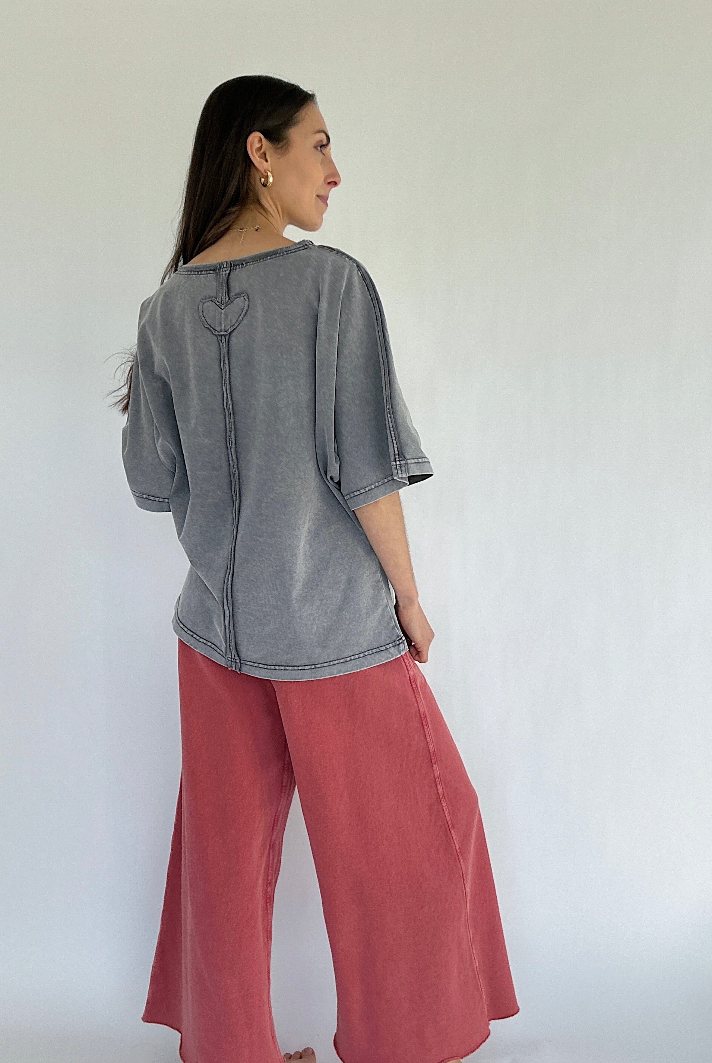 Woman wearing a gray top and pink pants against a white background showing the back