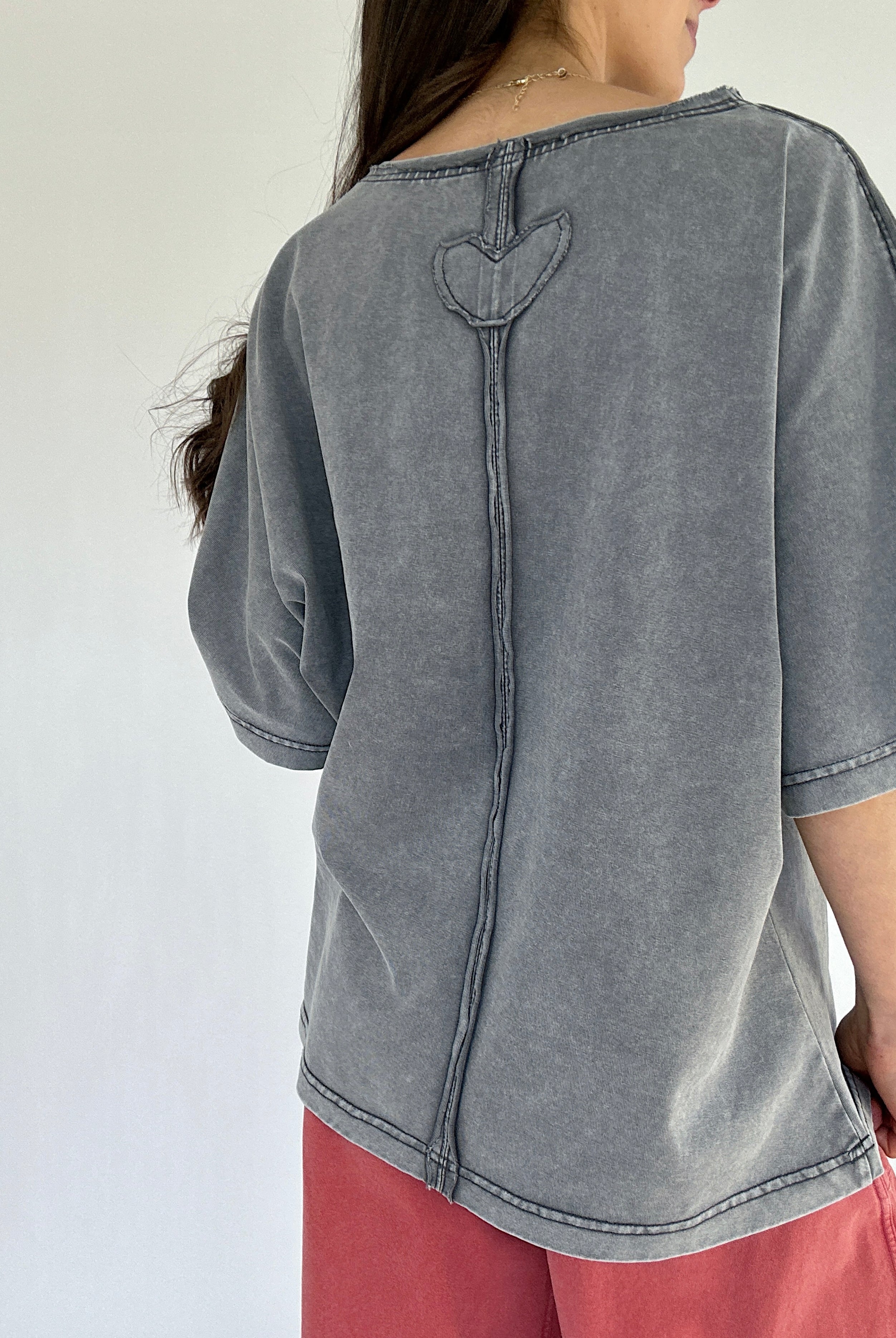 Person wearing a gray mineral washed top with a heart design on the back against a white background