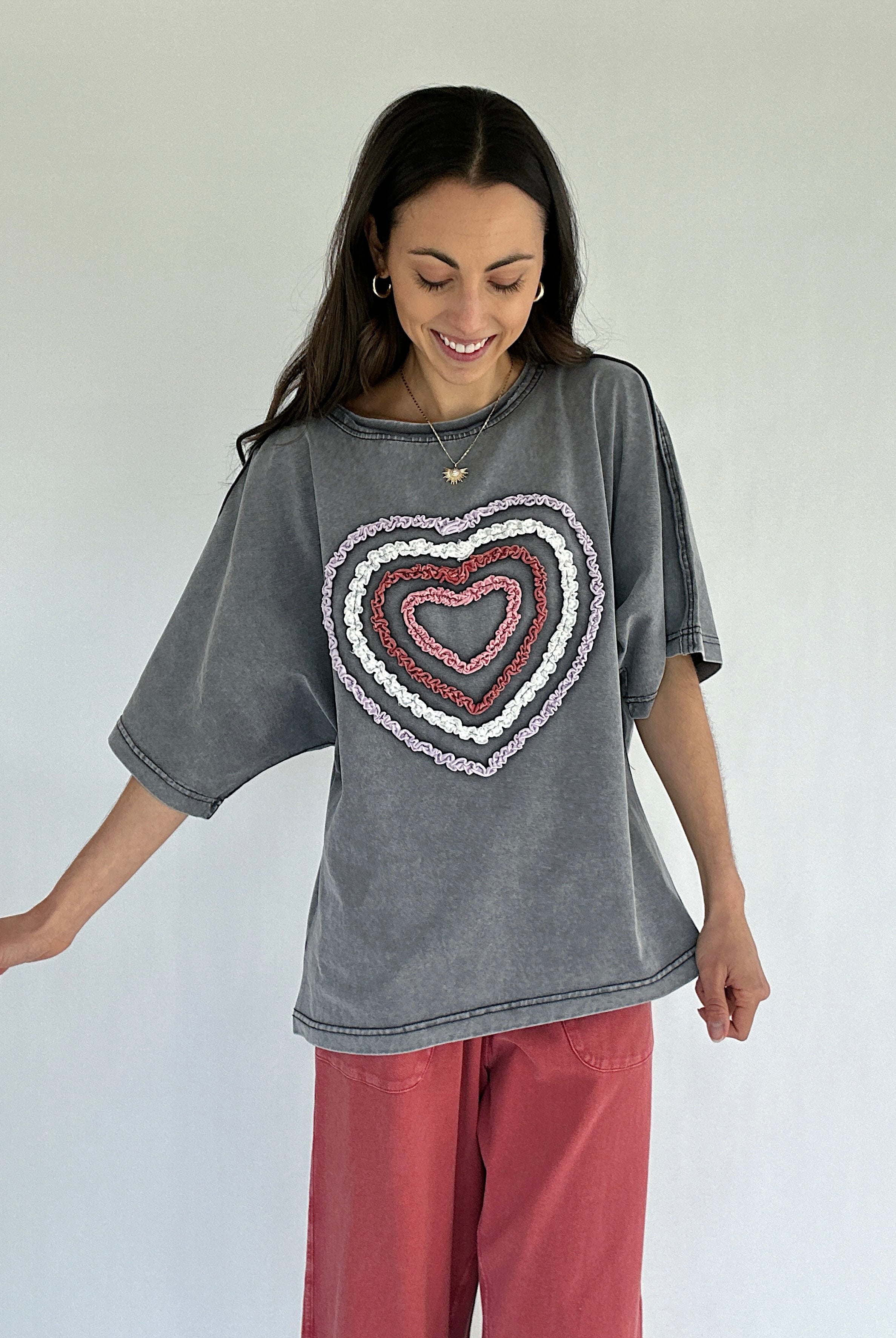 Woman wearing a gray t-shirt with a heart design on a plain background