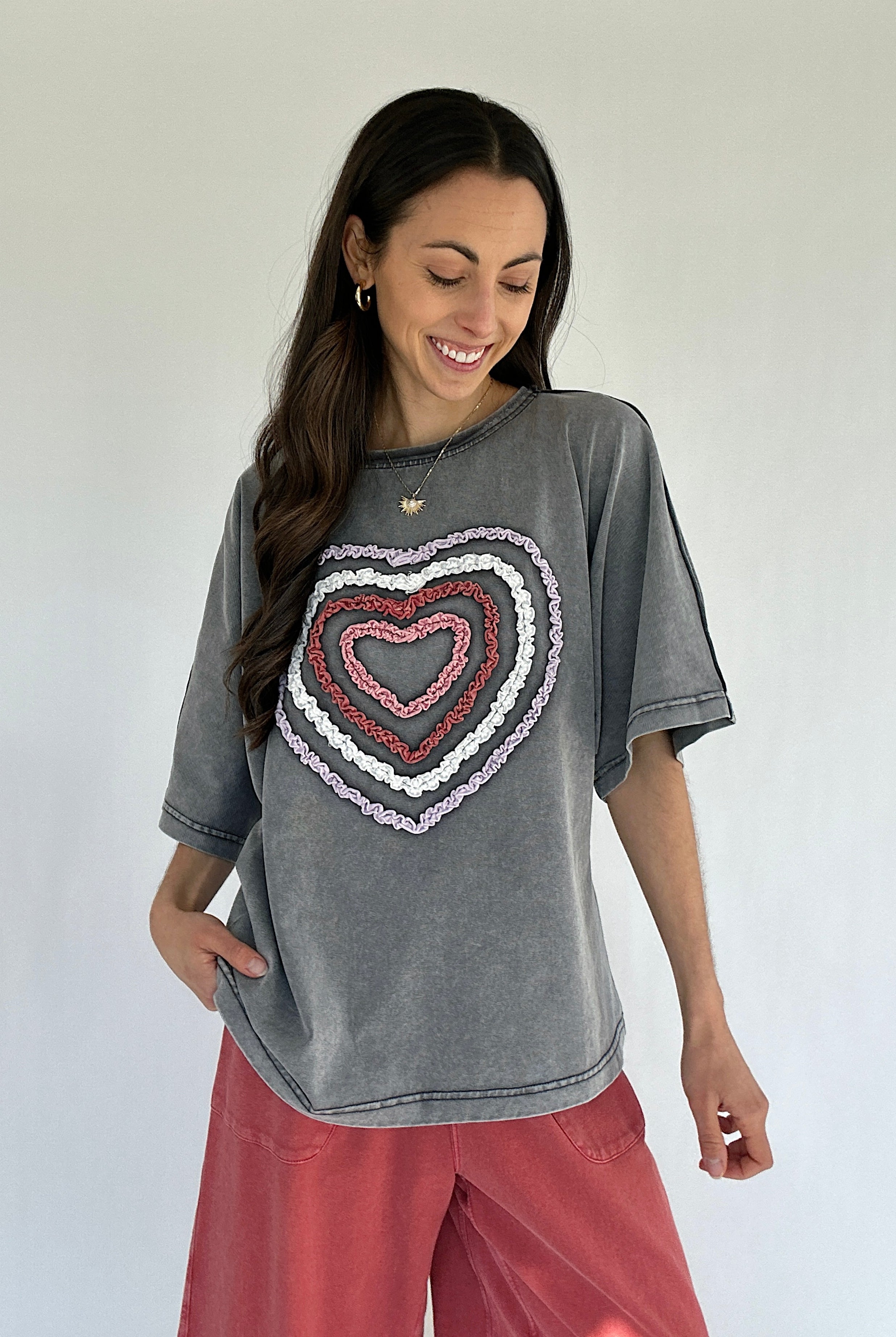 Woman wearing a gray t-shirt with a colorful heart design on a plain background