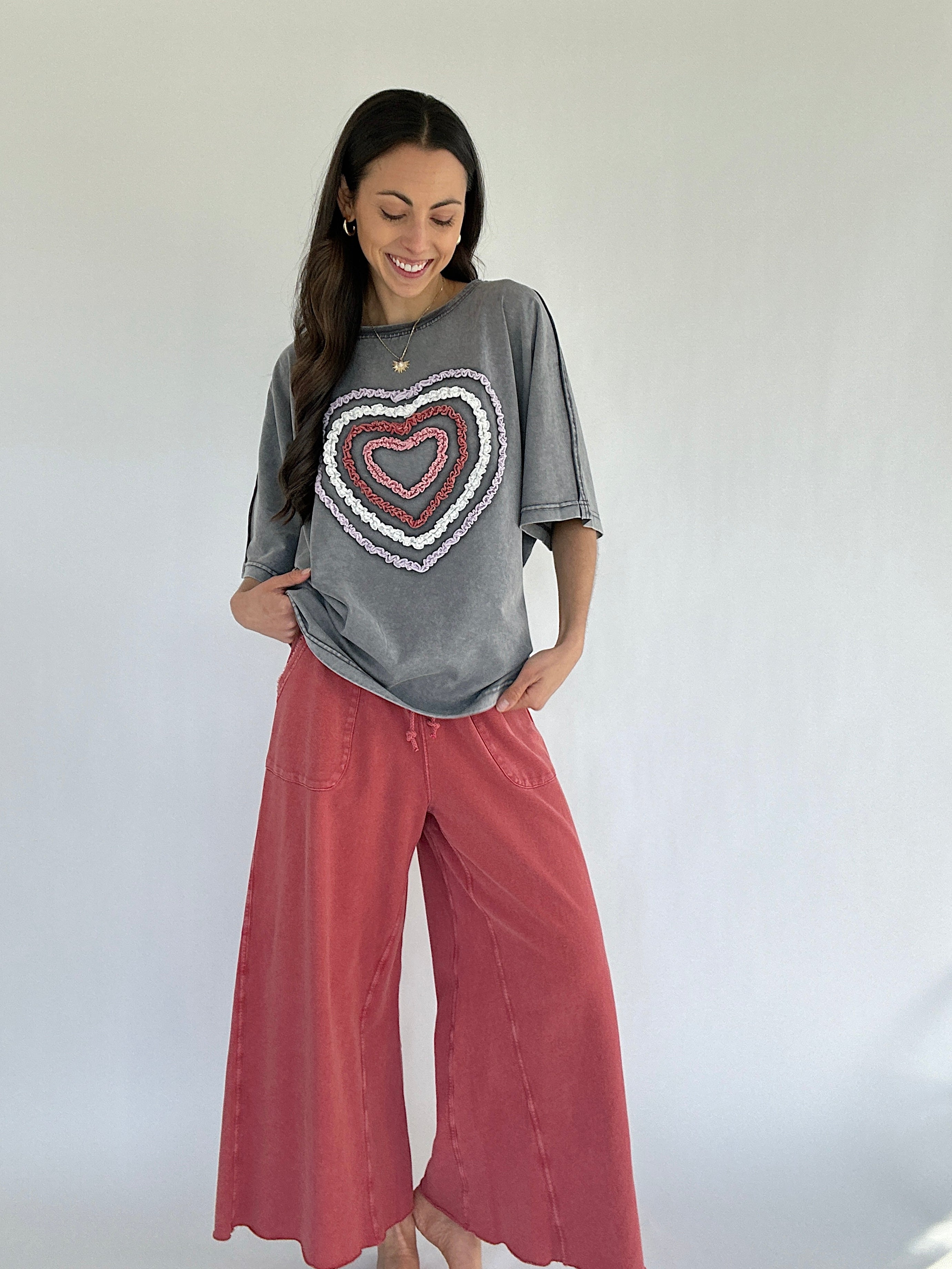 Woman wearing a gray t-shirt with a heart design and pink pants against a white background