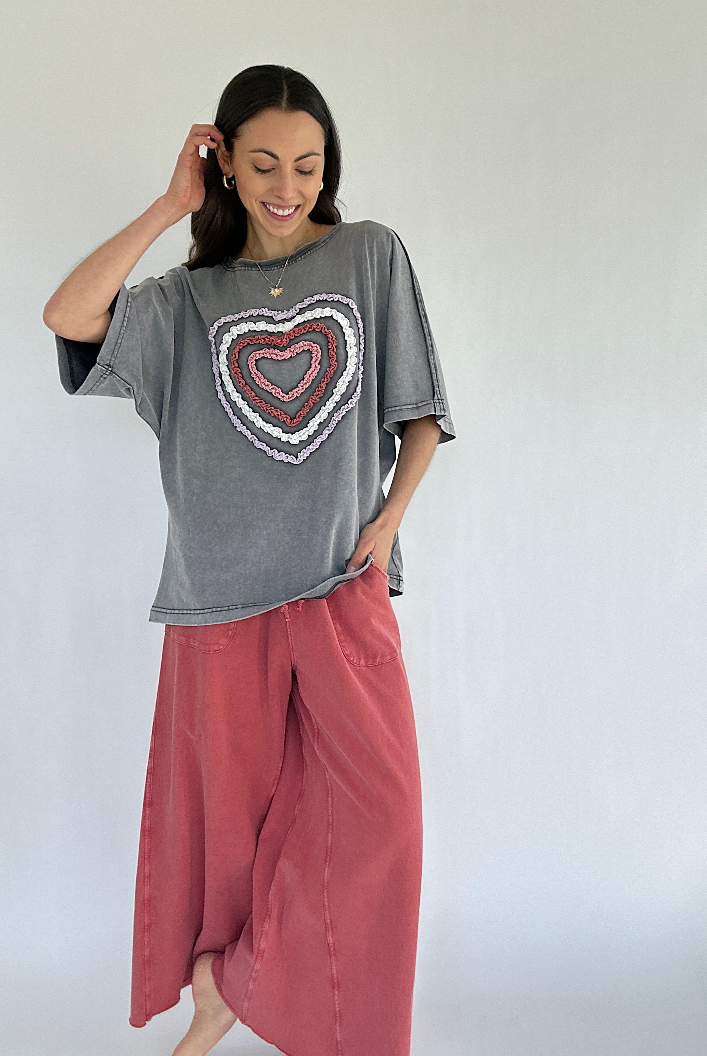 Woman wearing a gray t-shirt with a heart design and pink pants against a white background