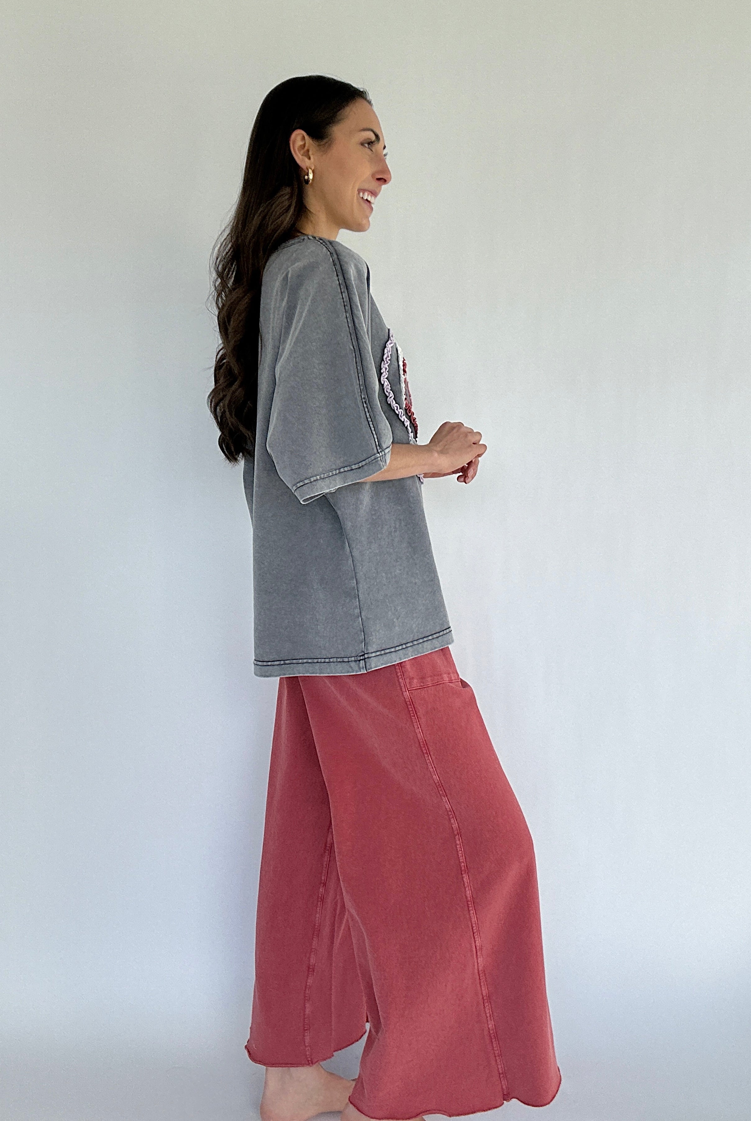 Woman wearing a gray oversized shirt and red pants against a white background from side
