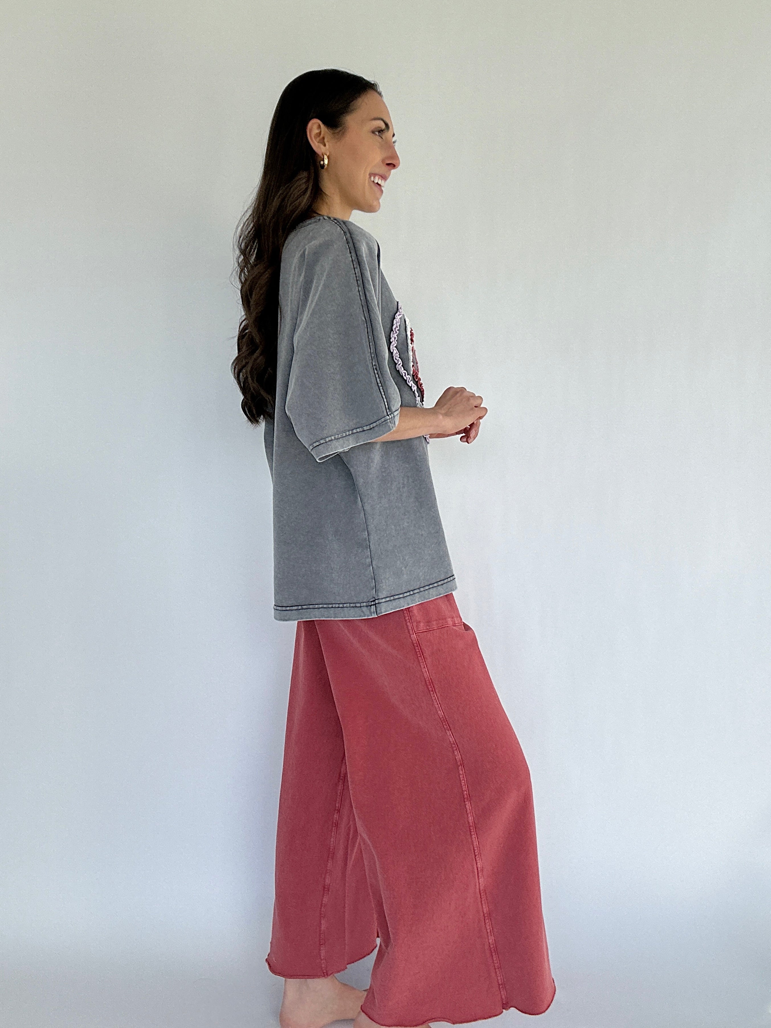 Woman wearing a gray oversized shirt and red pants against a white background from side