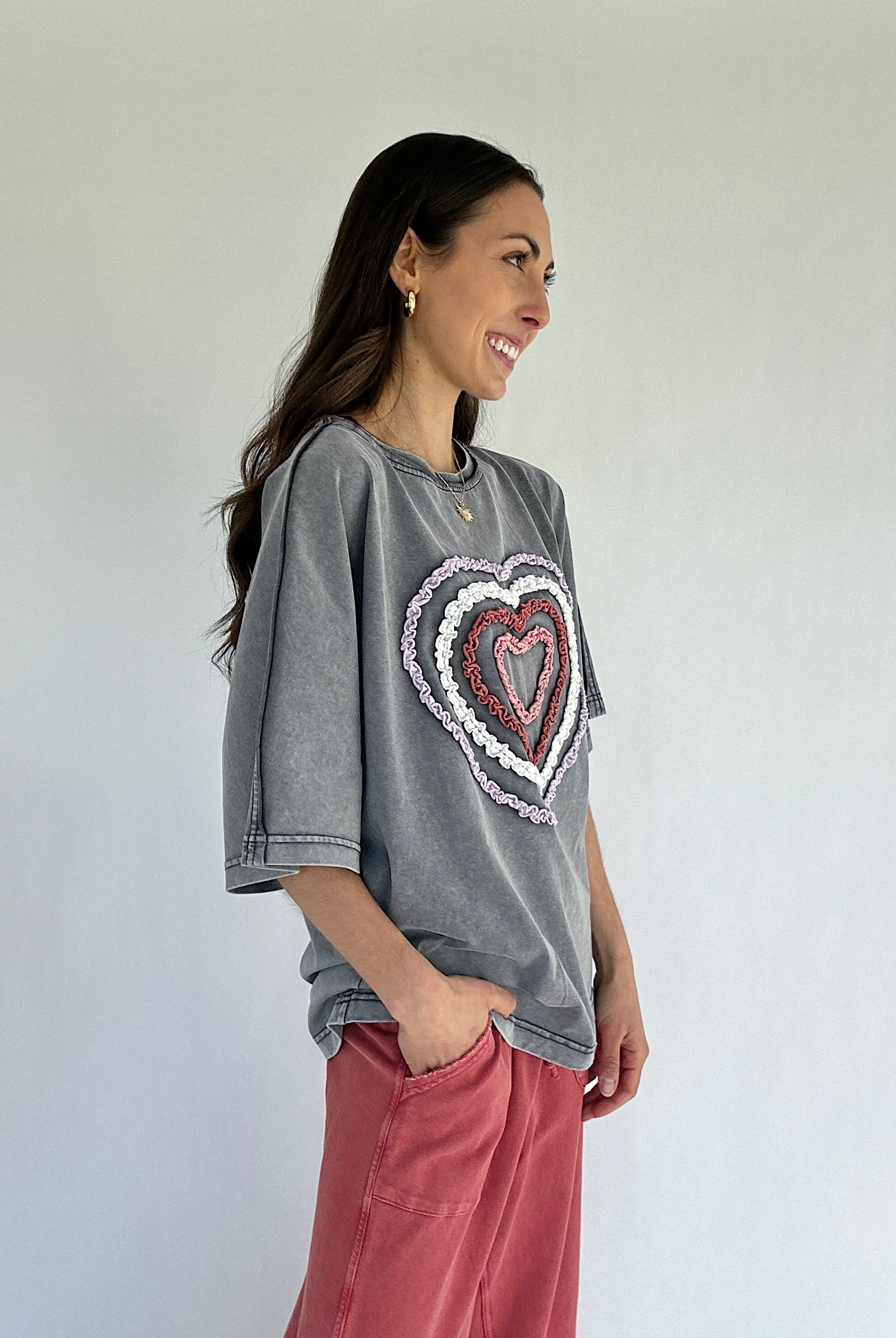 Woman wearing a gray oversized t-shirt with a heart design, standing against a plain background