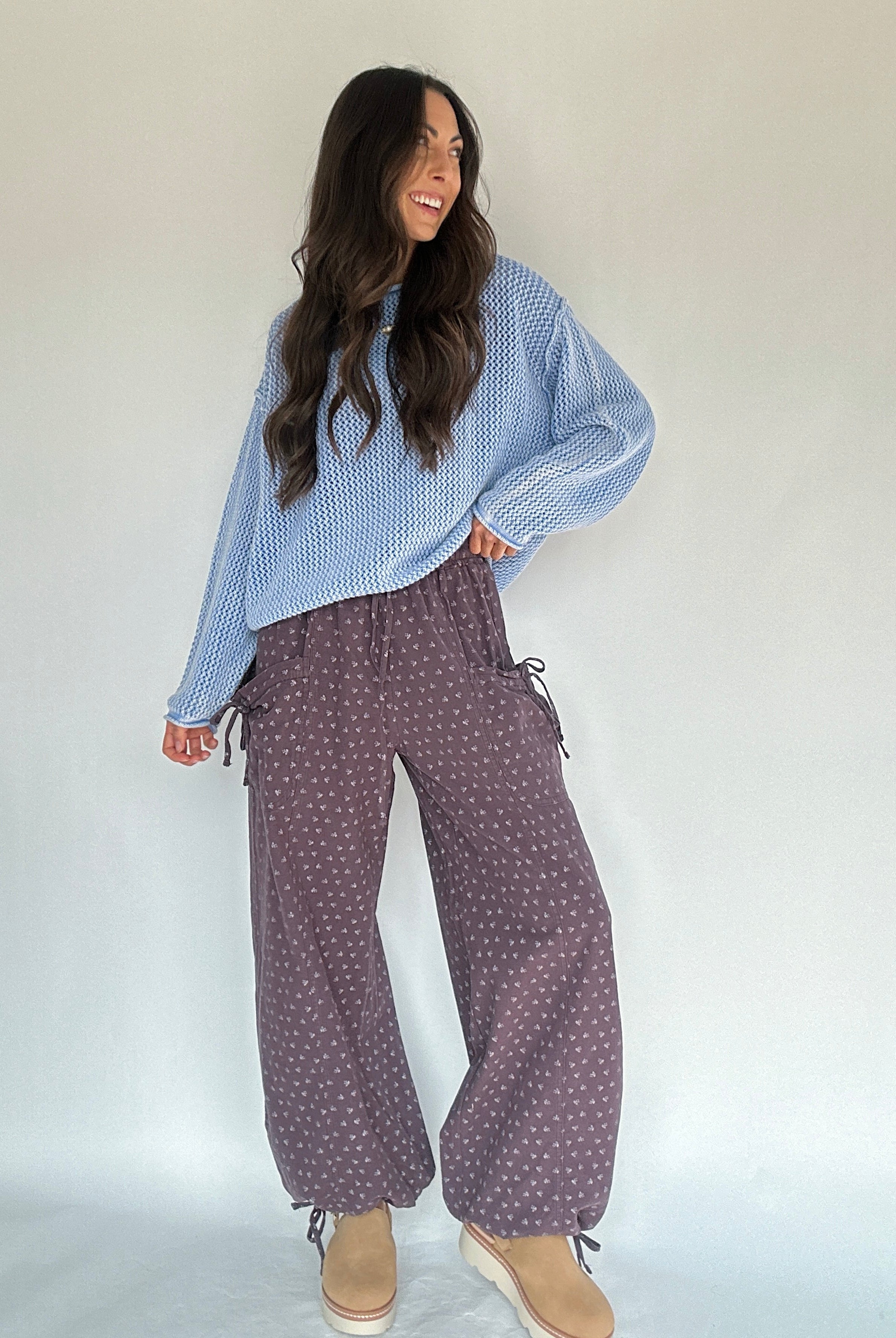 Woman wearing a blue patterned top and purple polka dot pants against a white background