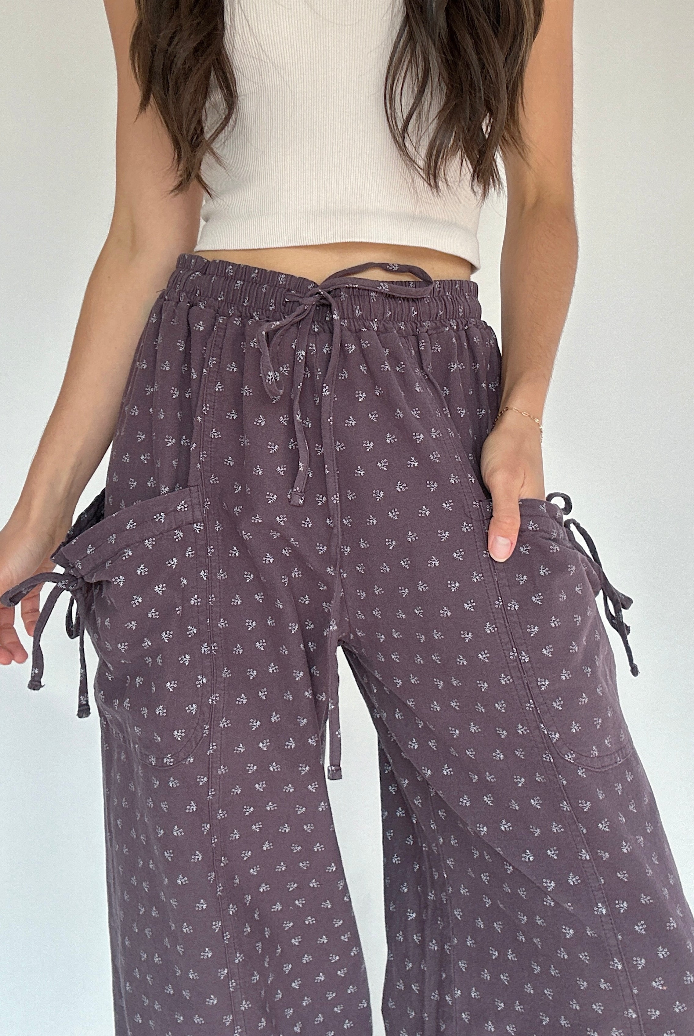 Person wearing purple patterned pants with a white top on a plain background showing up close waistband and pocket detail