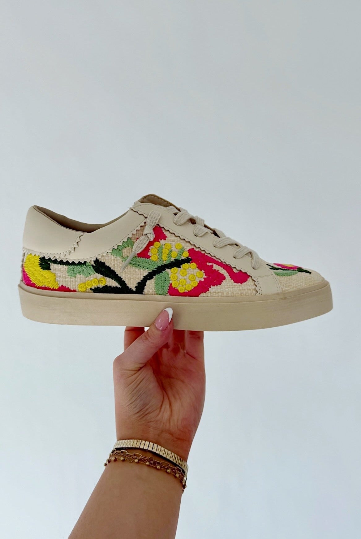 Hand holding a sneaker with floral embroidery against a light background
