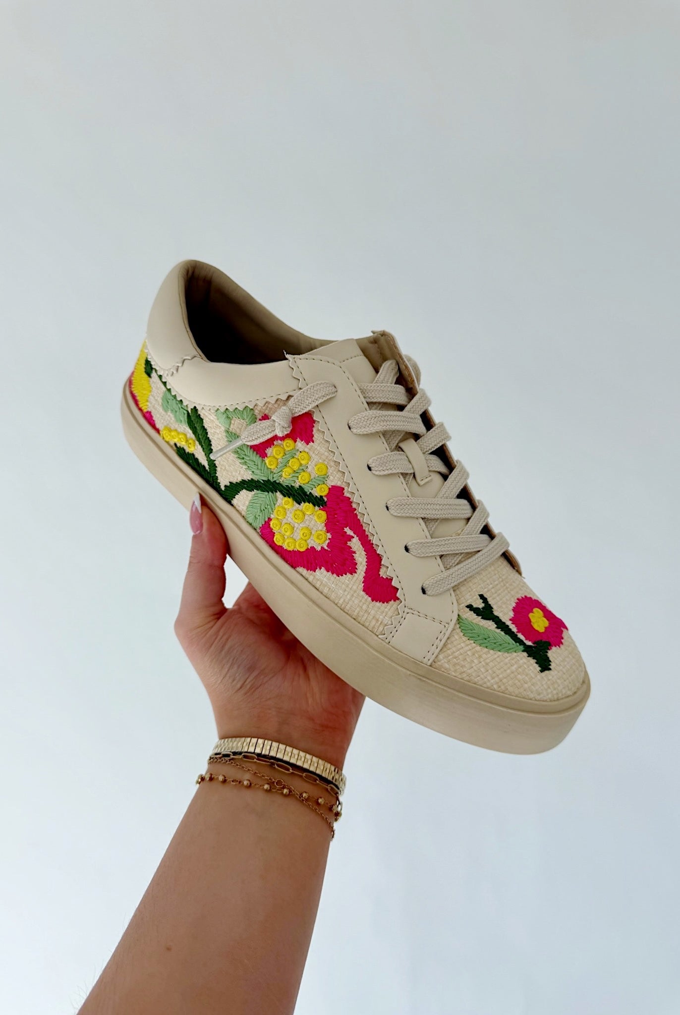 Beige sneaker with floral embroidery held by a hand against a light background