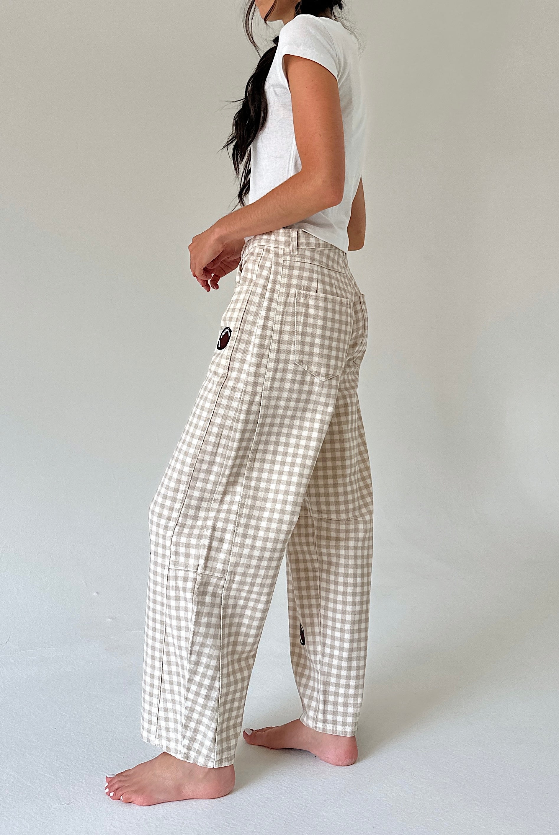 A woman wearing beige and white gingham wide-leg pants with a white t-shirt, shown from a side profile against a plain light gray studio background.