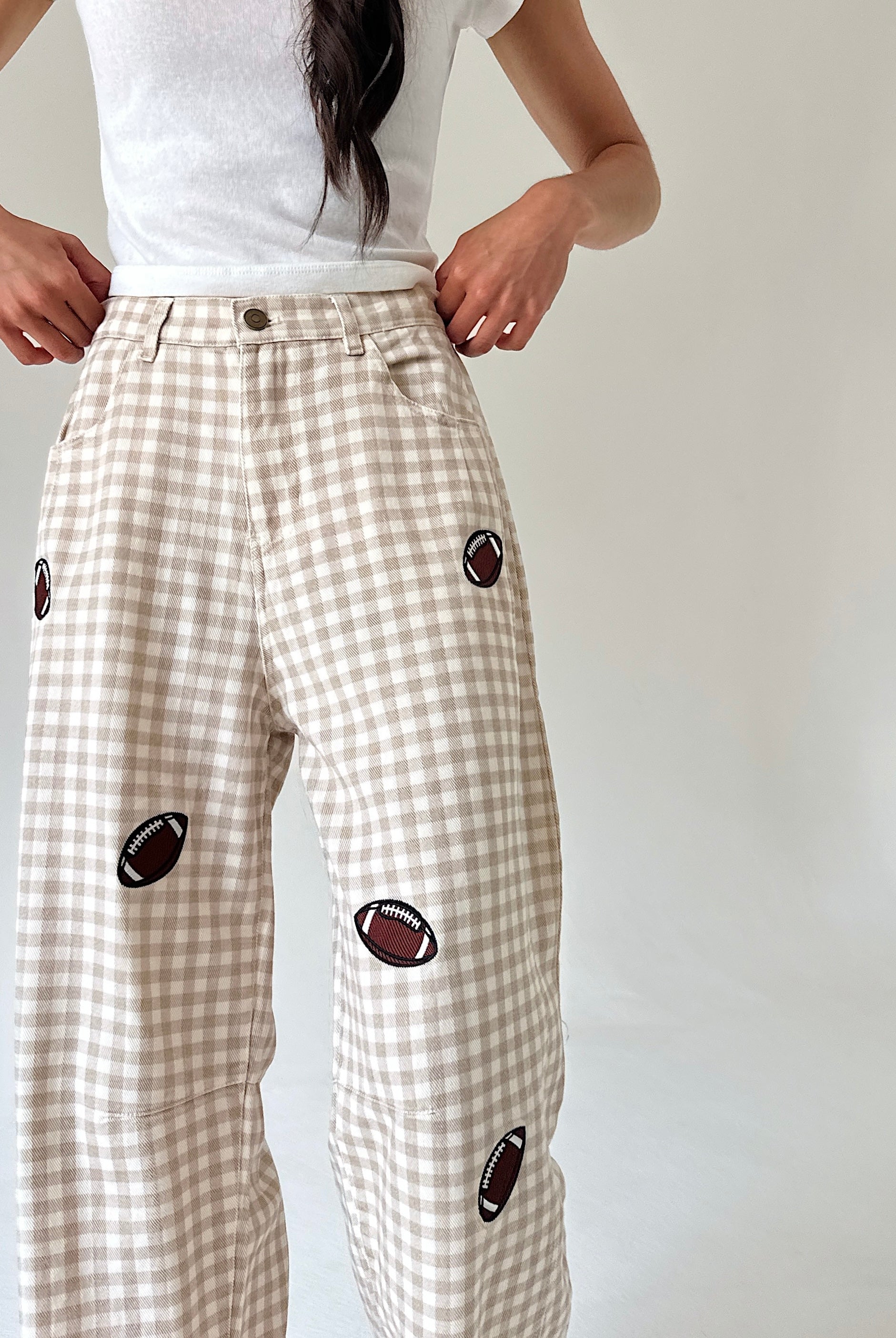 A person wearing beige and white gingham wide-leg pants with embroidered football patches, paired with a white t-shirt, shown from the waist down against a plain light background.