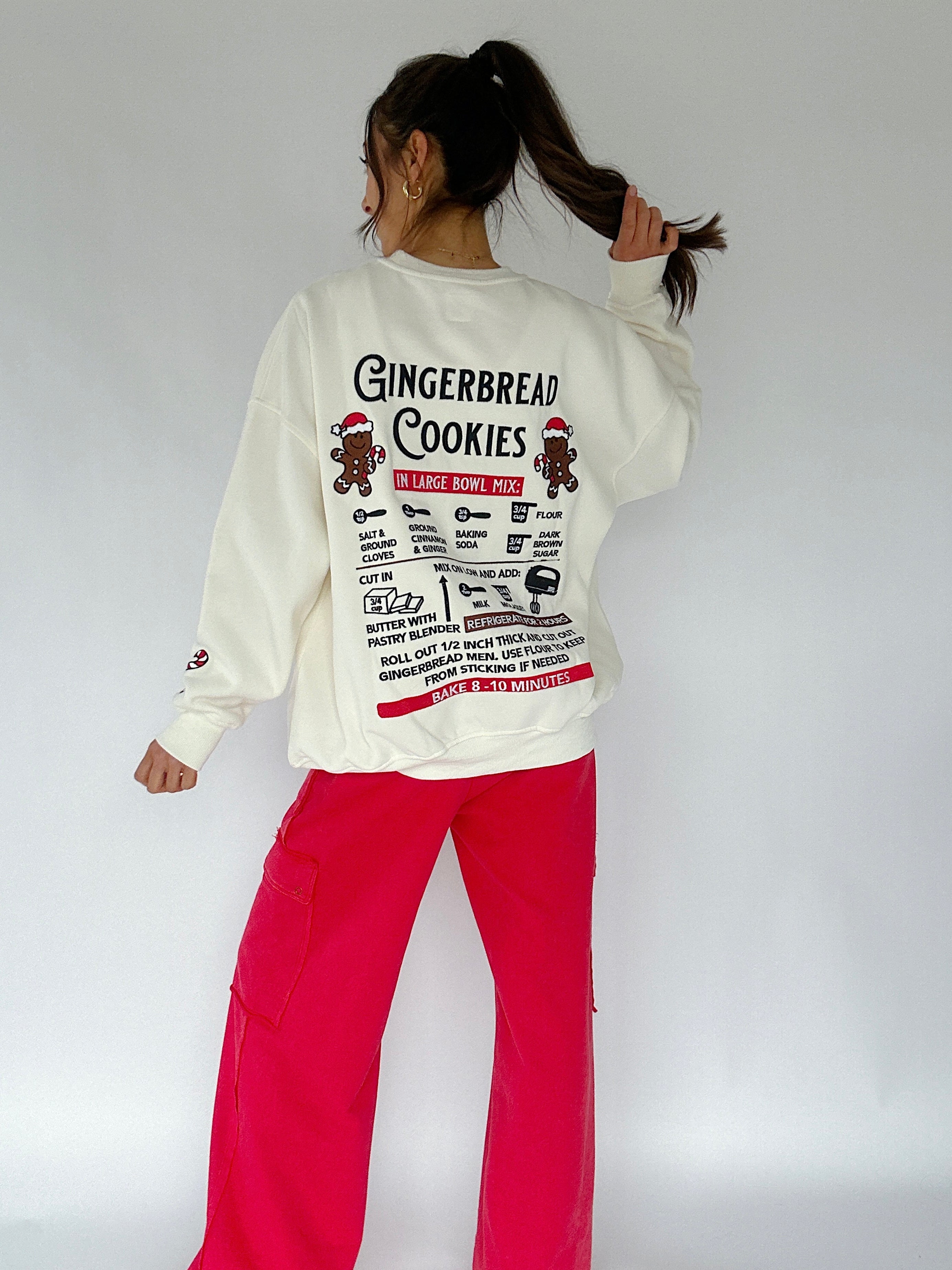 Person wearing a white sweatshirt with gingerbread recipe embroidered on the back standing against a plain background