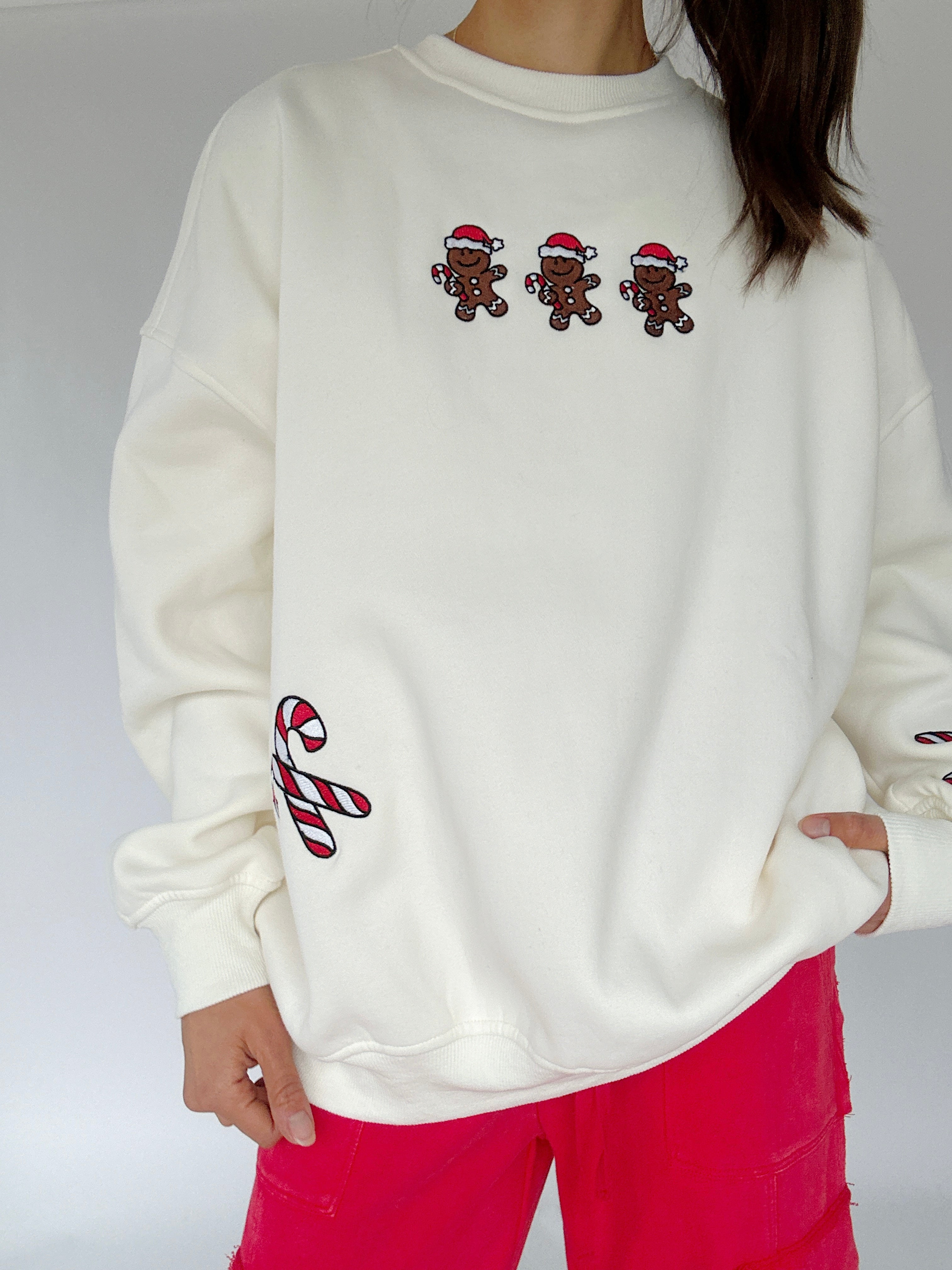 White sweatshirt with embroidered gingerbread men and candy canes on a plain background