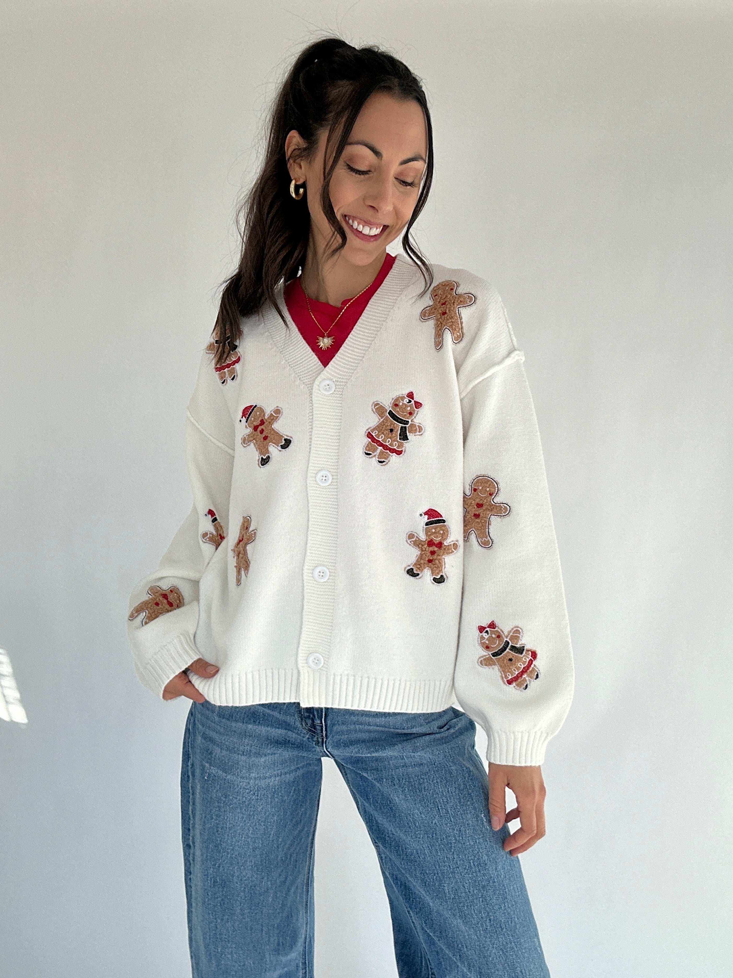 Woman wearing a white cardigan with gingerbread man patches on a plain background