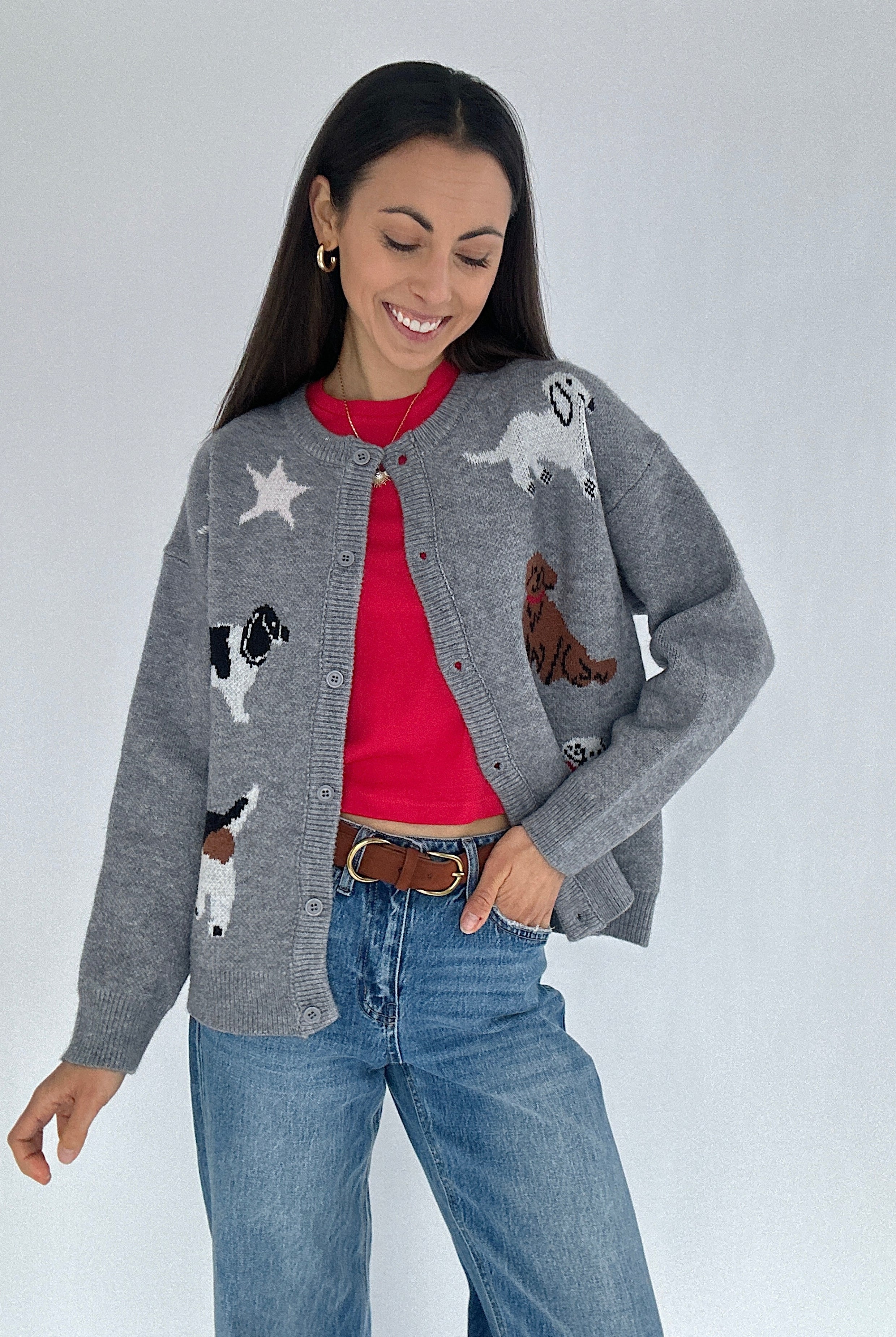 Woman wearing a gray cardigan with dog graphics over a red tee and jeans on a plain background