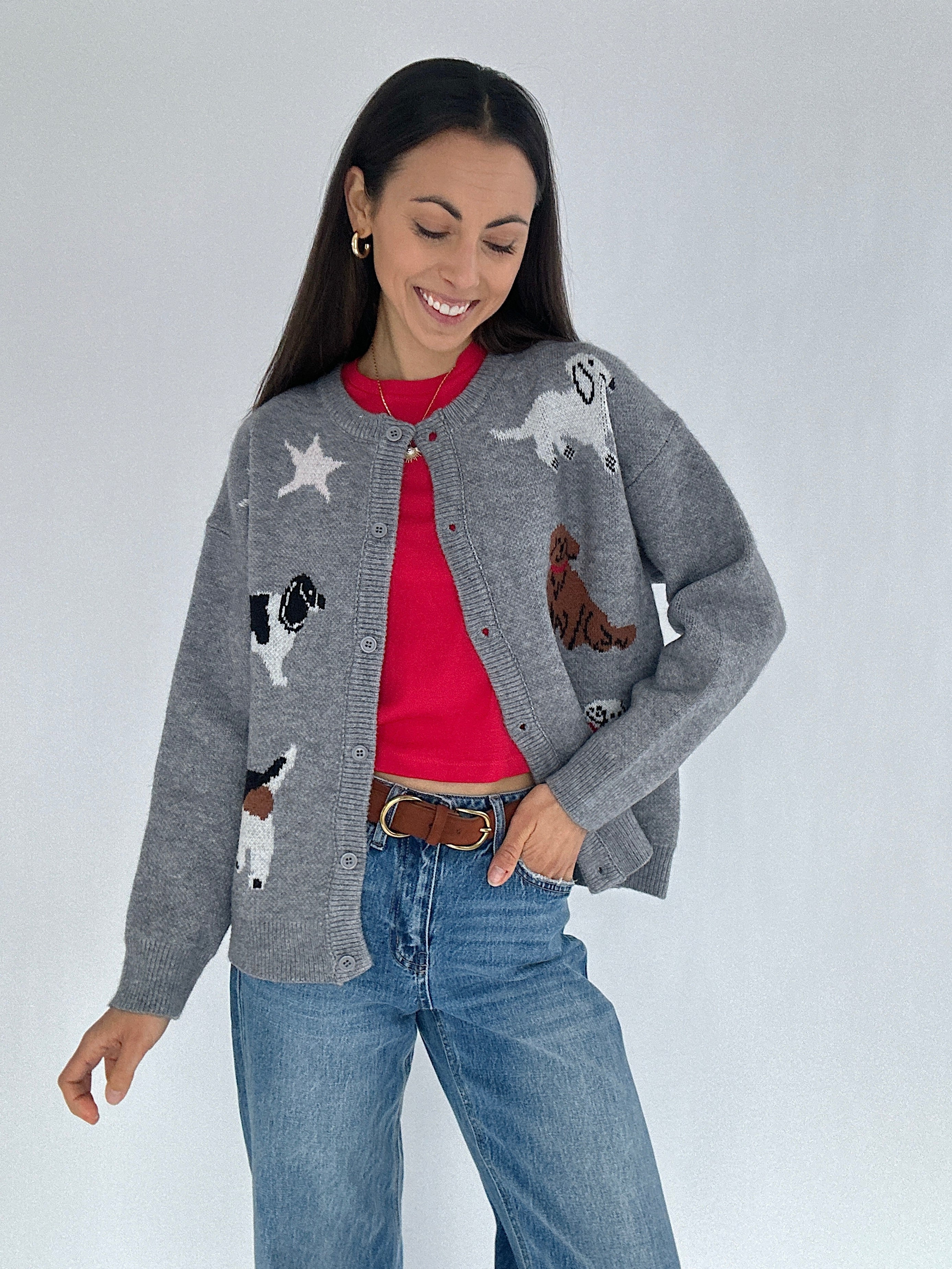 Woman wearing a gray cardigan with dog graphics over a red tee and jeans on a plain background