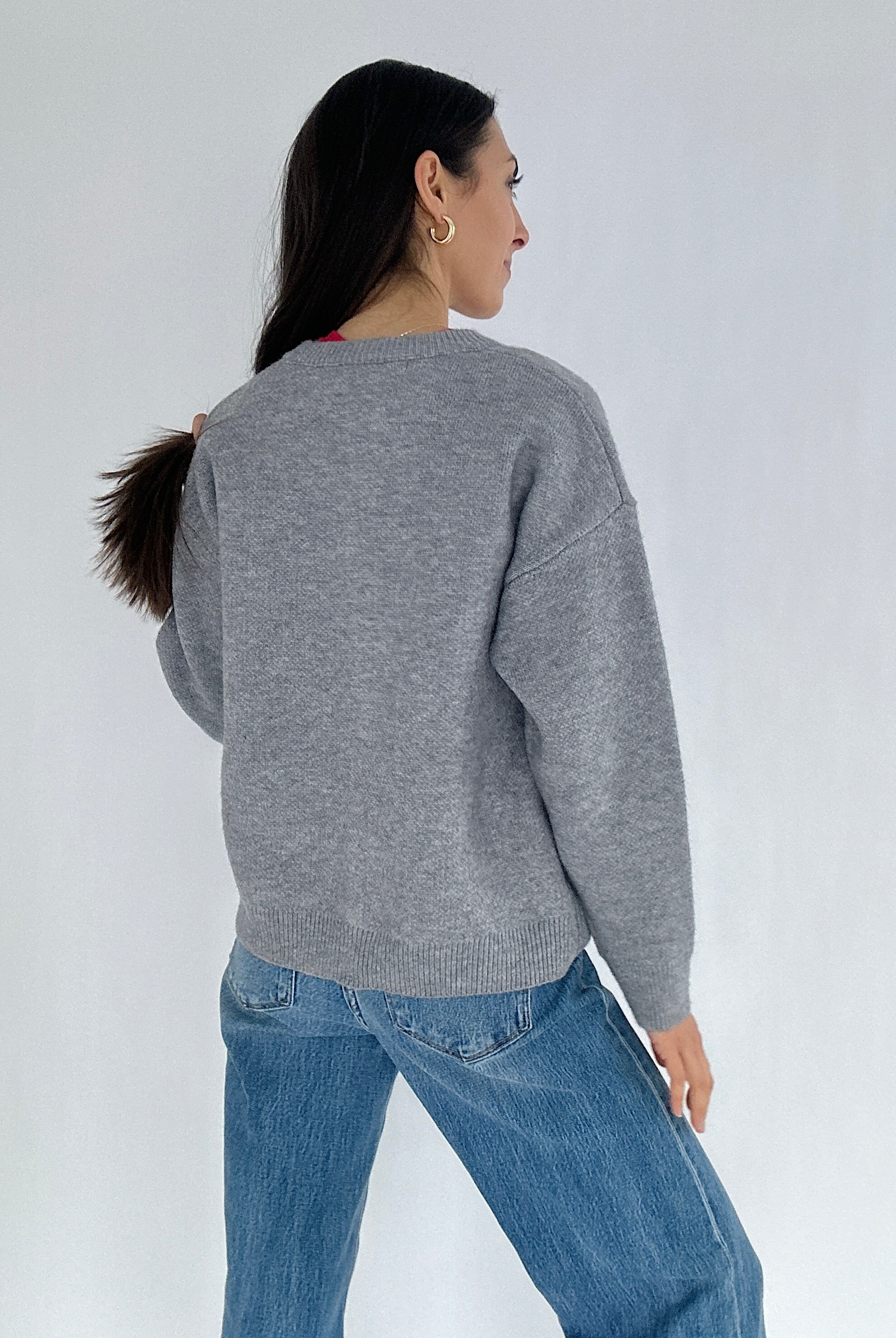 Person wearing a gray sweater and blue jeans on a white background showing the back