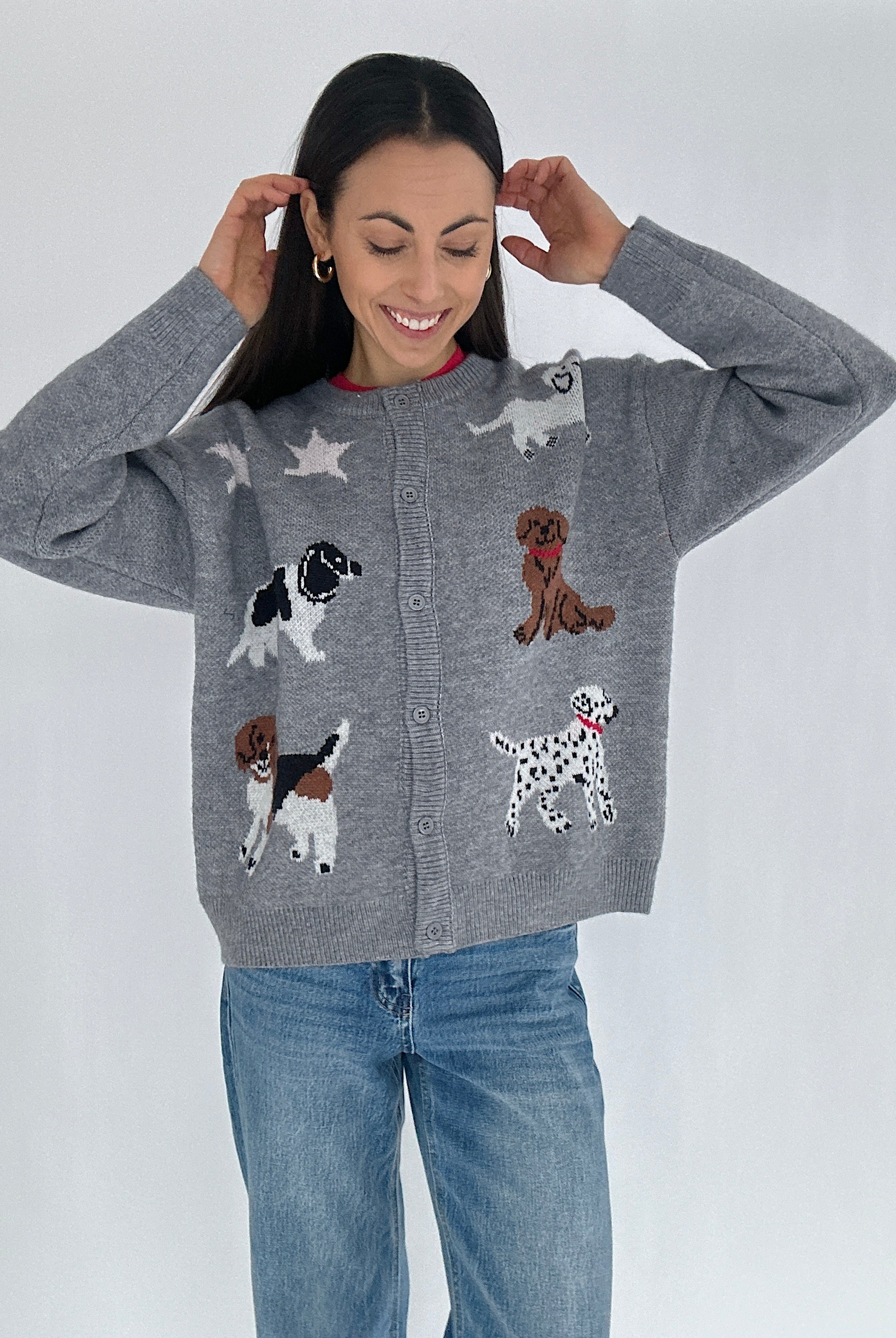 Woman wearing a gray cardigan sweater with dog illustrations buttoned with jeans on a white background